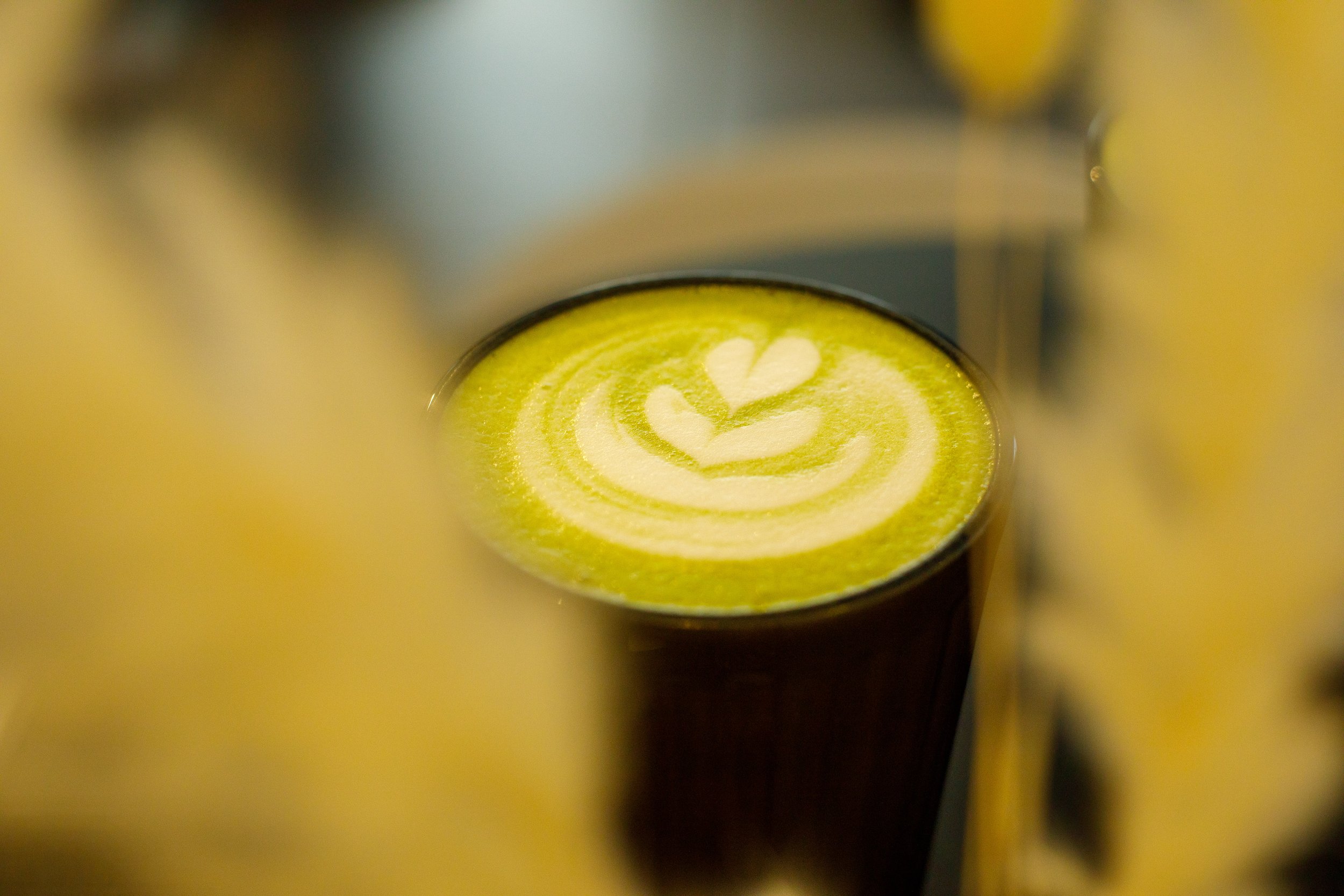 Un verre de latte avec un dessin en forme de cœur et de feuillage en mousse de lait vert brûlé.