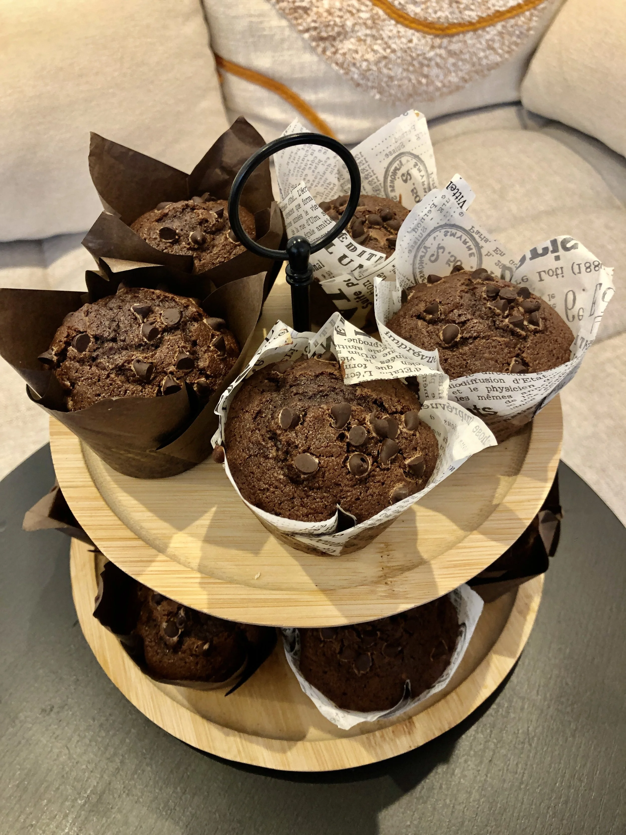 Assortiment de muffins au chocolat sur un plateau en bois à deux niveaux, avec en arrière-plan le fauteuil du café.