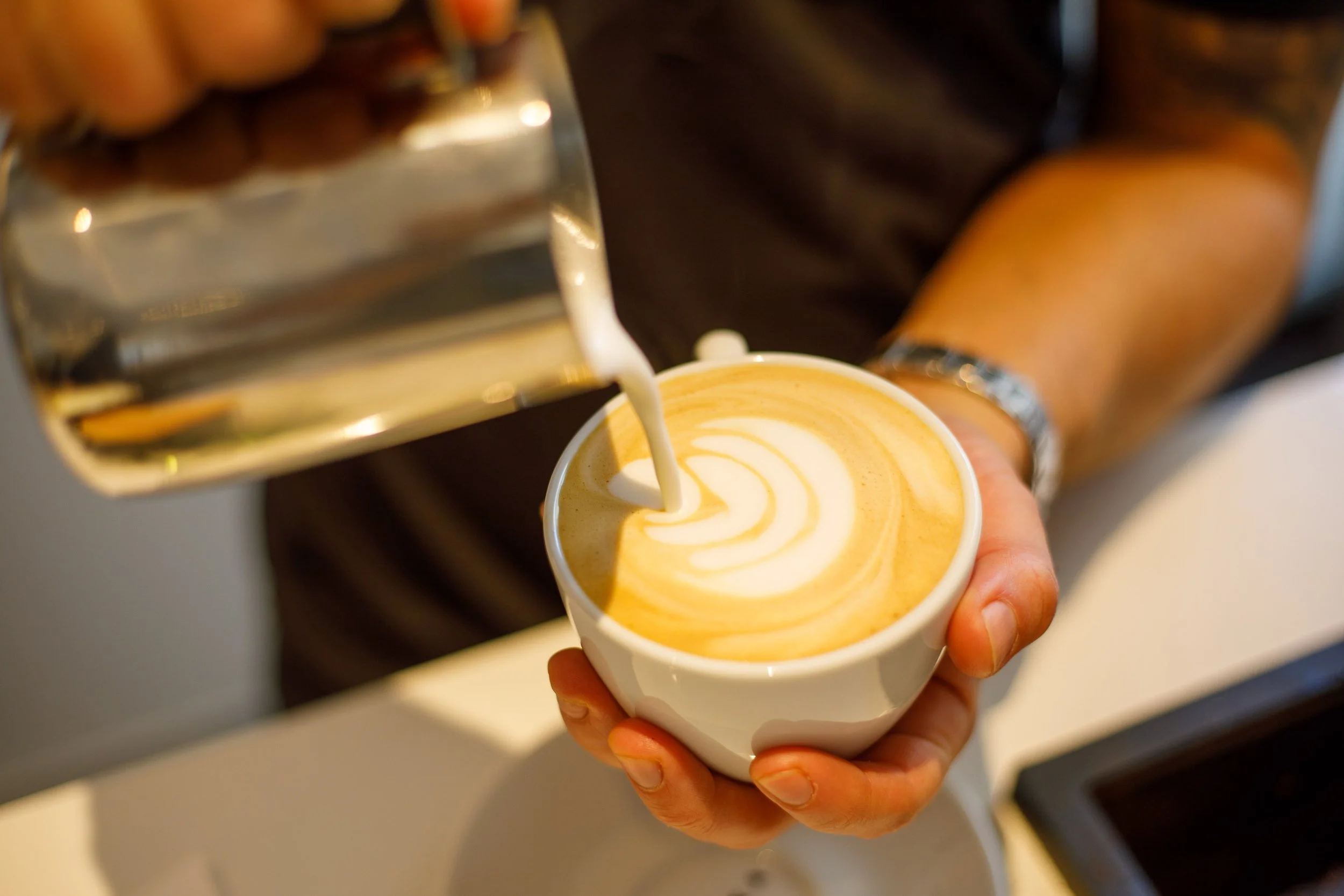 Un barista verse du lait chaud pour faire un latte dans une tasse blanche.