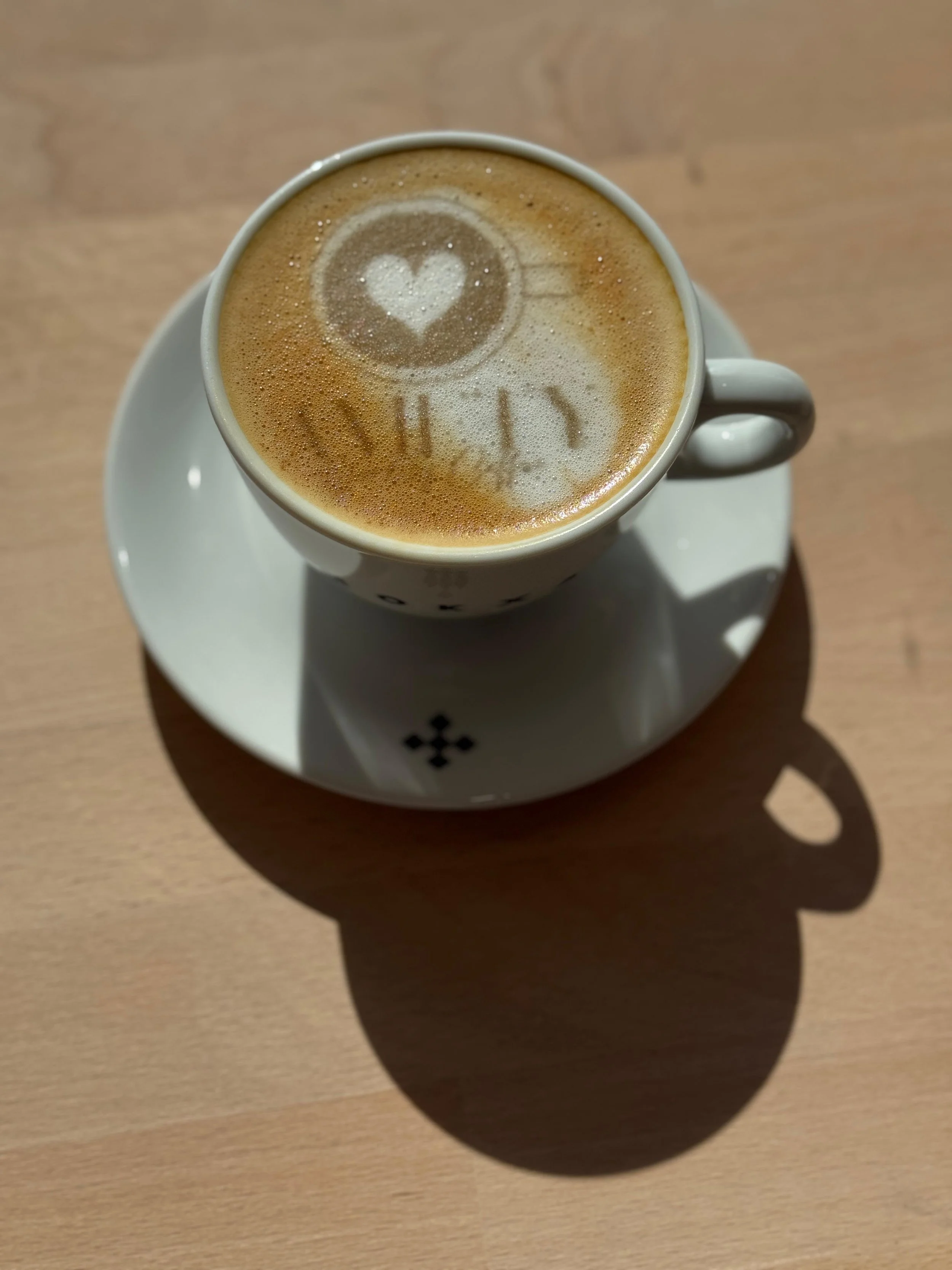 Tasse de café avec dessin en forme de cœur et de tasse de café sur la mousse, vue du dessus, posée sur une assiette blanche sur une table en bois.