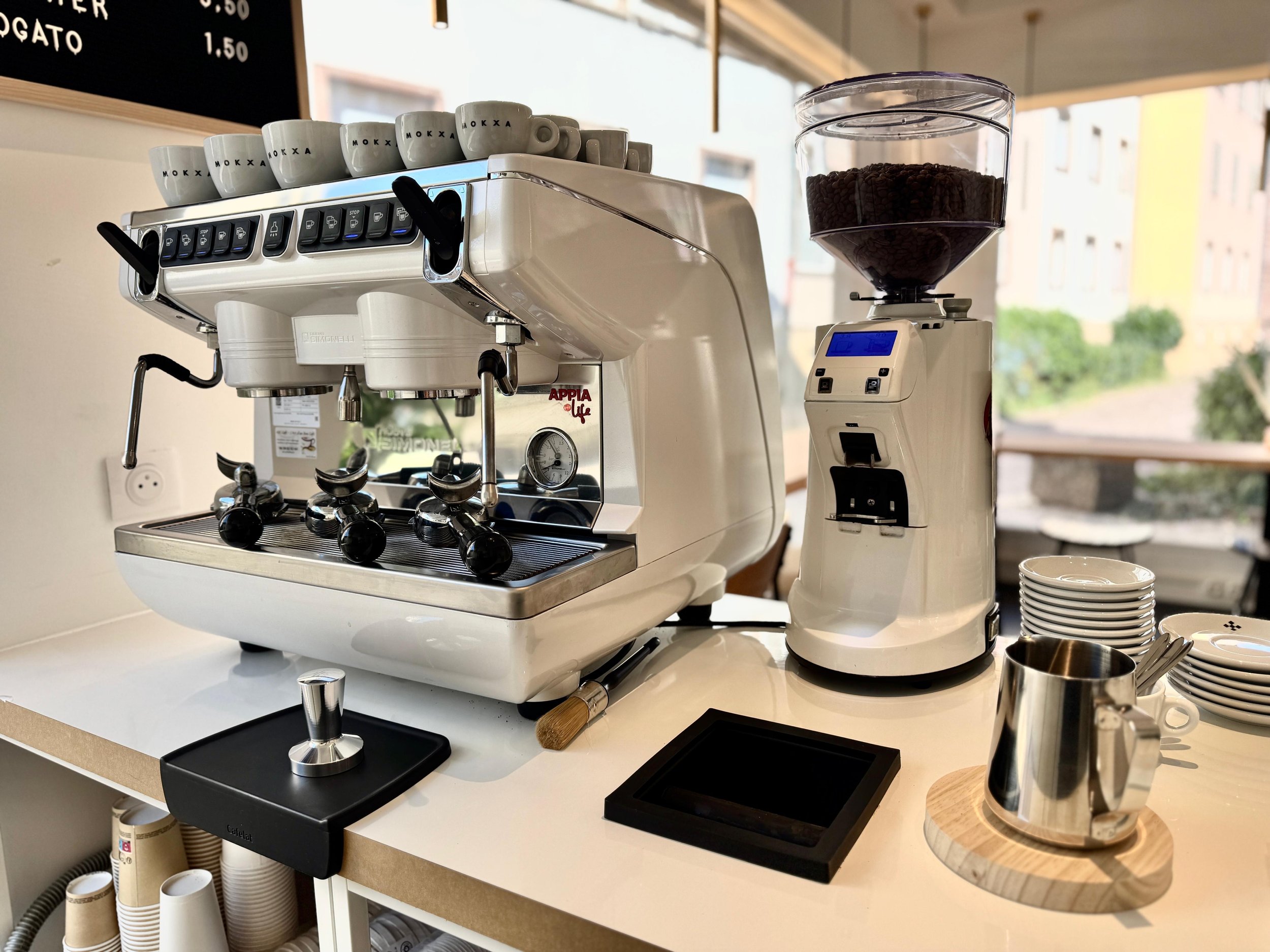 Machine à espresso avec tasses sur le dessus, moulin à café à côté, et tasses empilées à côté, dans un café