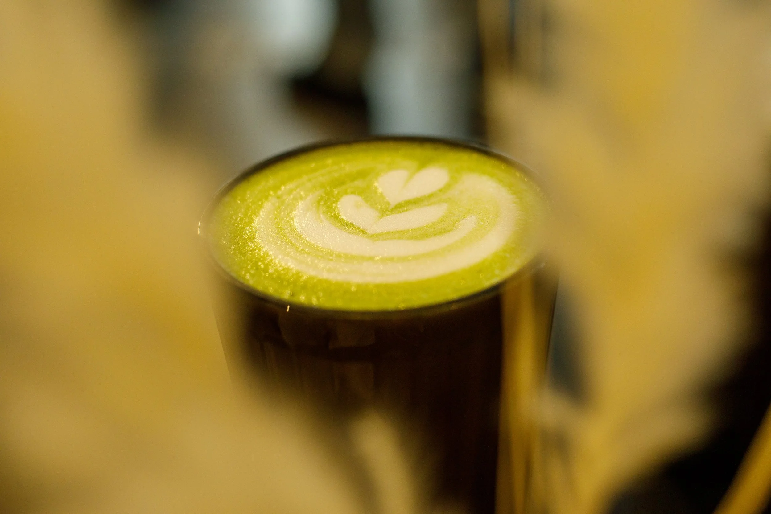 Matcha latte avec un motif en forme de cœur et de feuilles dans la mousse. En premier plan flou des herbes de pampa.