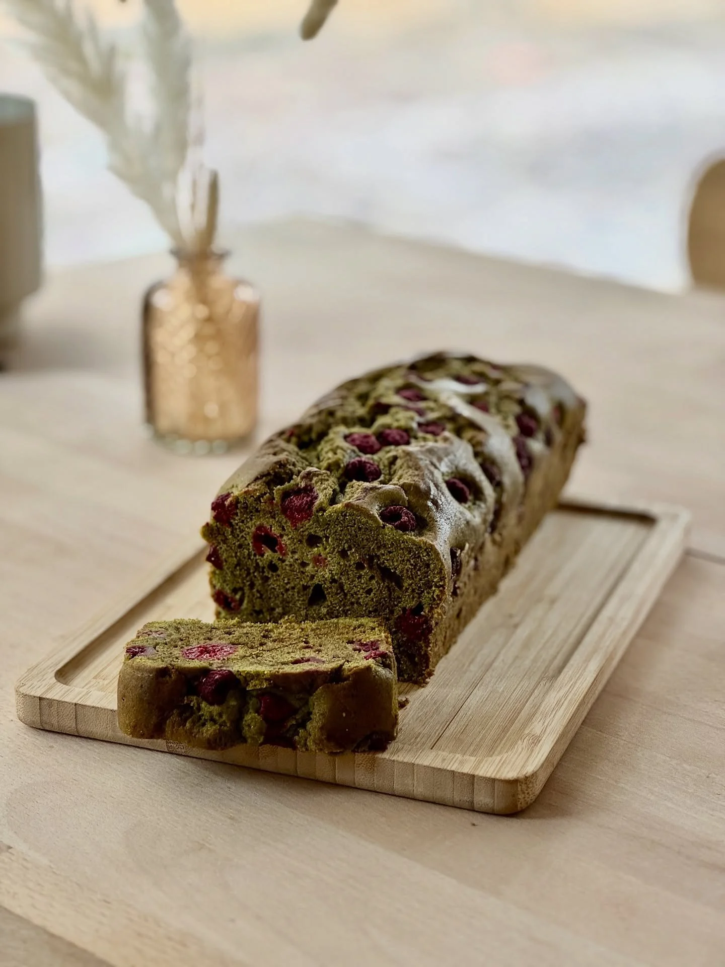 Cake à la pistache et aux framboises sur une planche en bois, sur une table en bois avec des décorations d'herbes séchées.