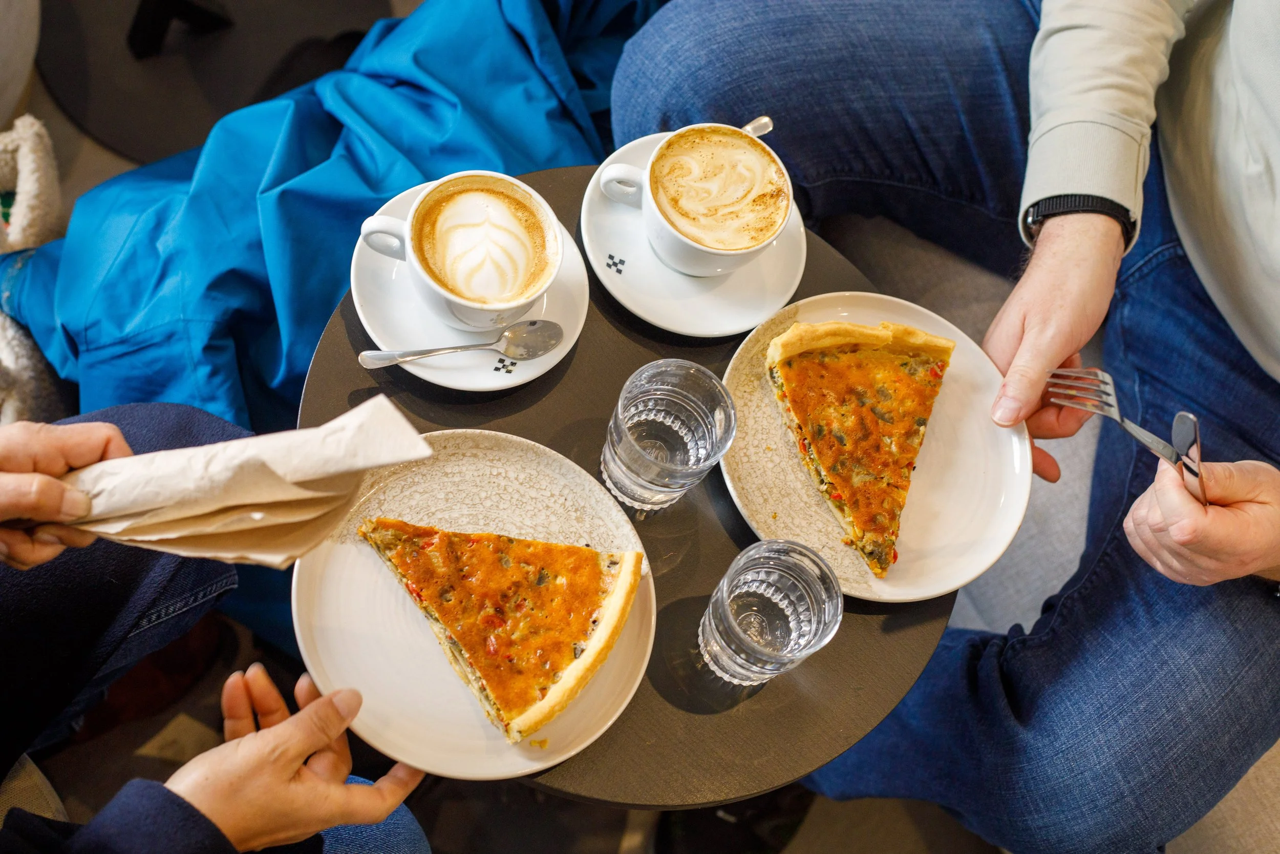 Deux personnes prennent une pause avec deux parts de pizza, deux cafés latte, deux verres d'eau sur une table ronde dans un café.