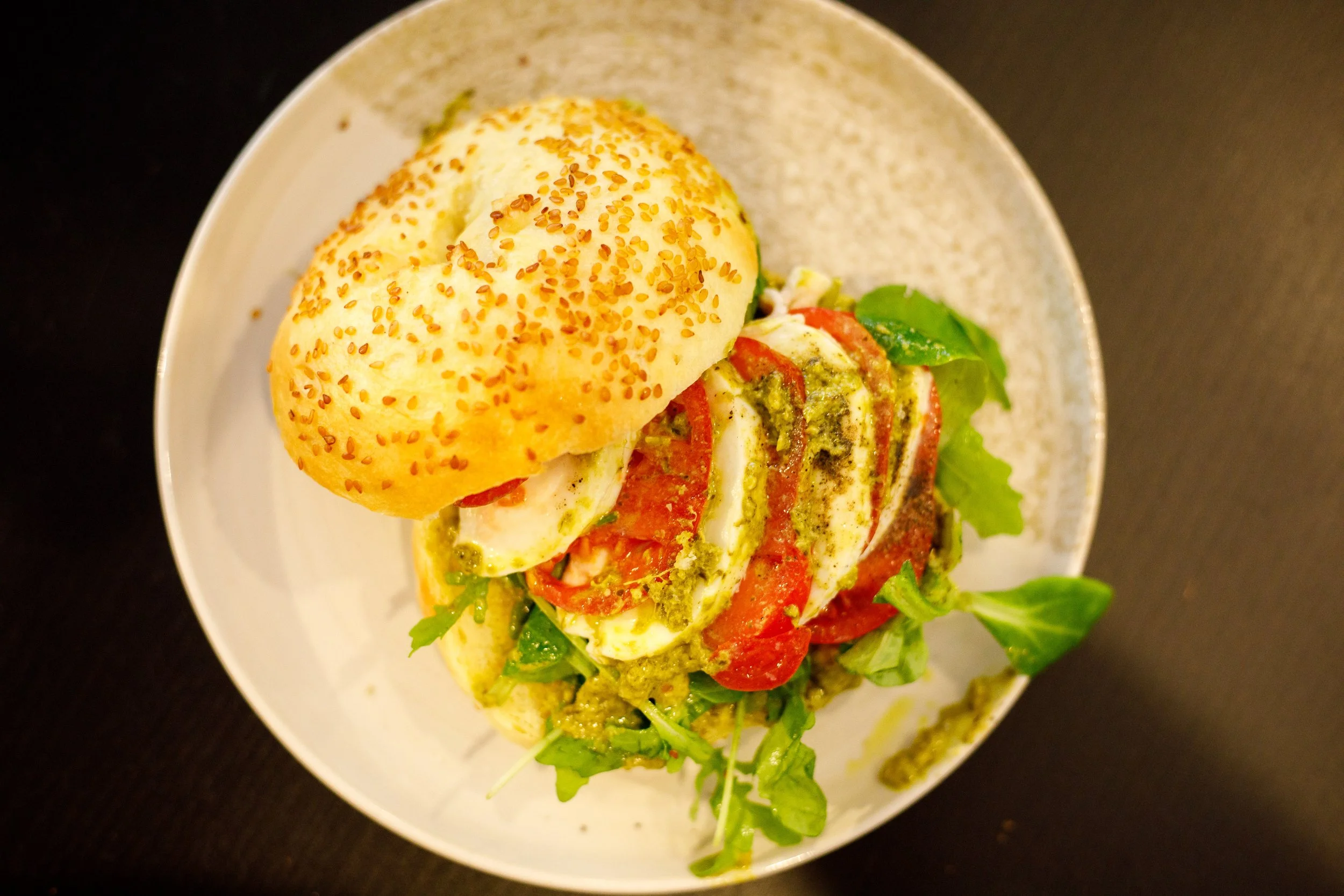 Sandwich avec tomates, mozzarella, pesto, laitue, avec un petit pain bagel saupoudré de graines de sésame.