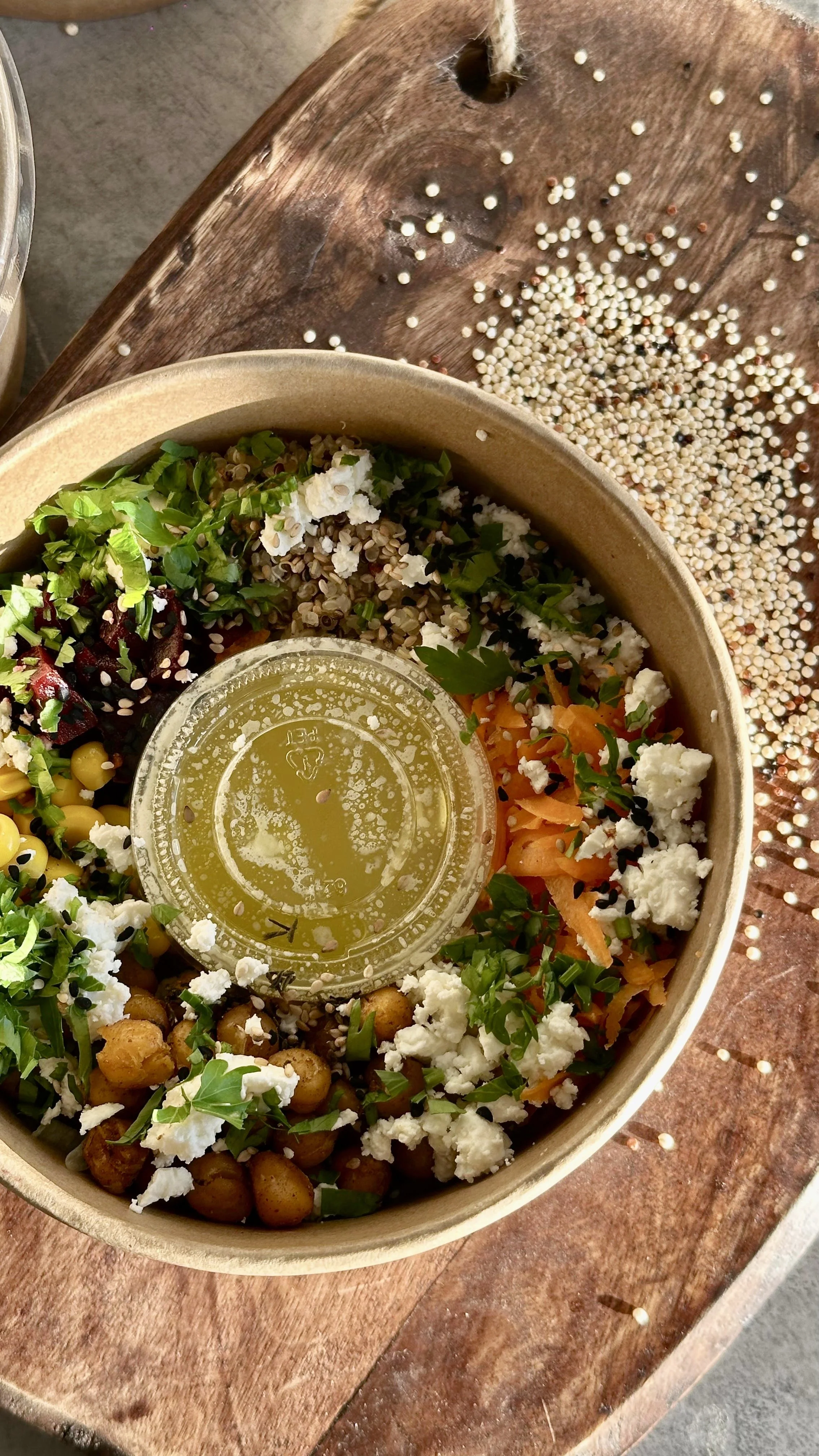 Salade composée avec pois chiches grillés, carottes râpées, betteraves, fromage feta, herbes, et une vinaigrette maison avec de la moutarde au centre, sur une table en bois.