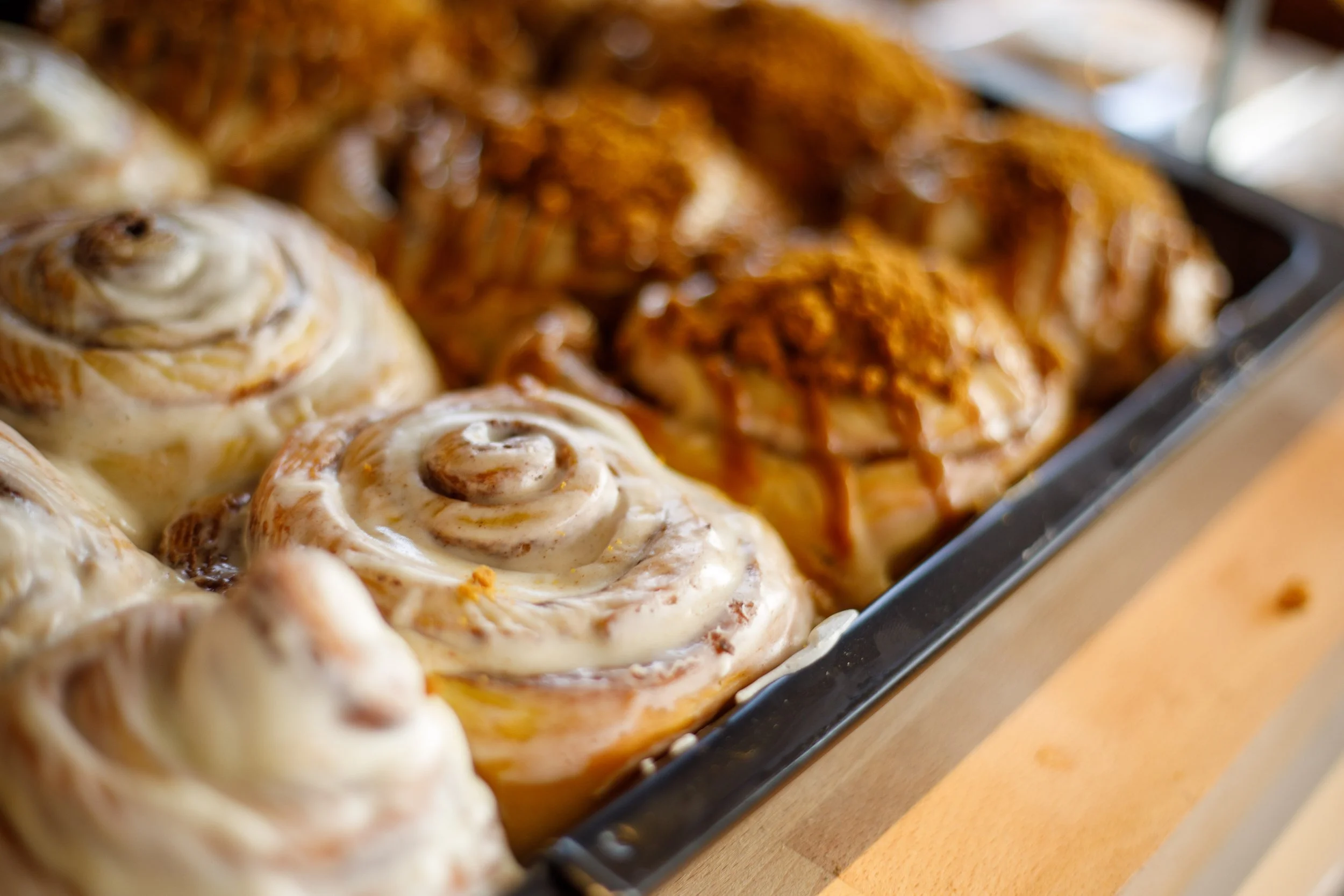 Gros plan sur des pâtisseries, notamment des viennoiseries comme des rouleaux à la cannelle recouverts de glaçage blanc et des pâtisseries avec une garniture croustillante et un filet de caramel.