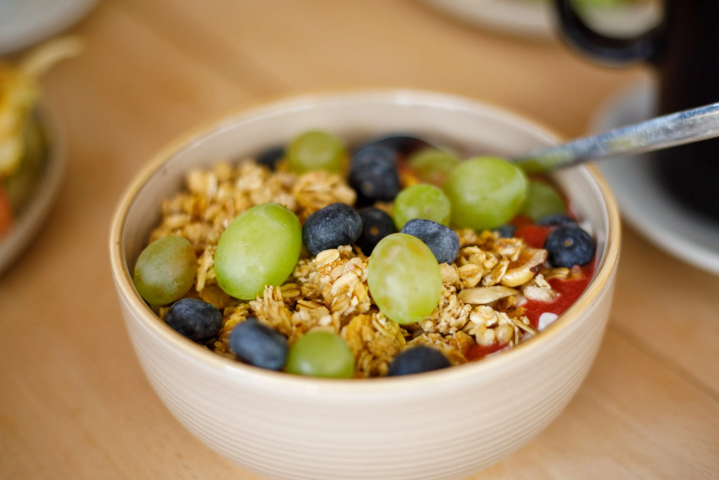 Bol de granola avec des raisins verts et des myrtilles sur une table.