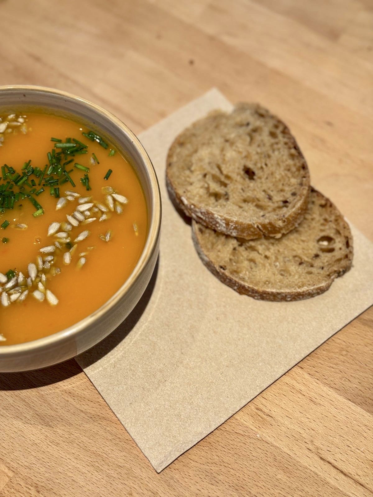 Soupe à la courge, garnie de graines et de ciboulette, accompagnée de tranches de pain complet.