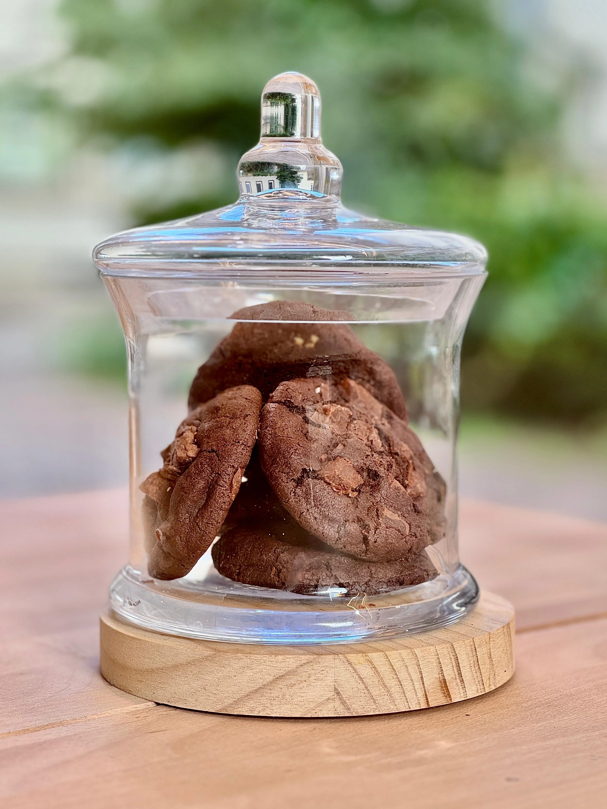 Biscuits au chocolat dans une jarre en verre avec couvercle en verre, posé sur une base en bois, sur une surface en bois.