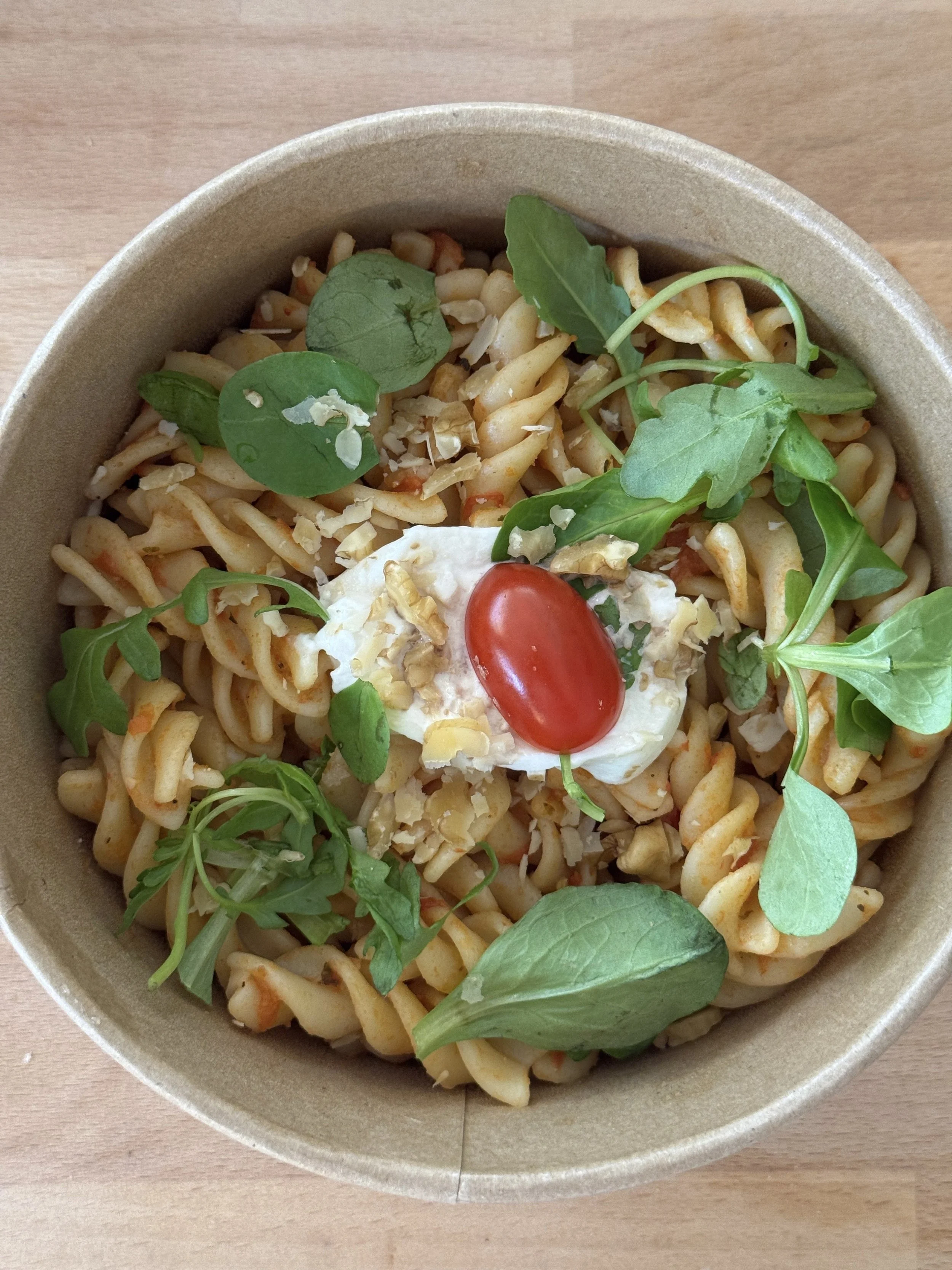 Bol de salade de pâtes avec tomates cerises, salade, pesto, et mozzarella.