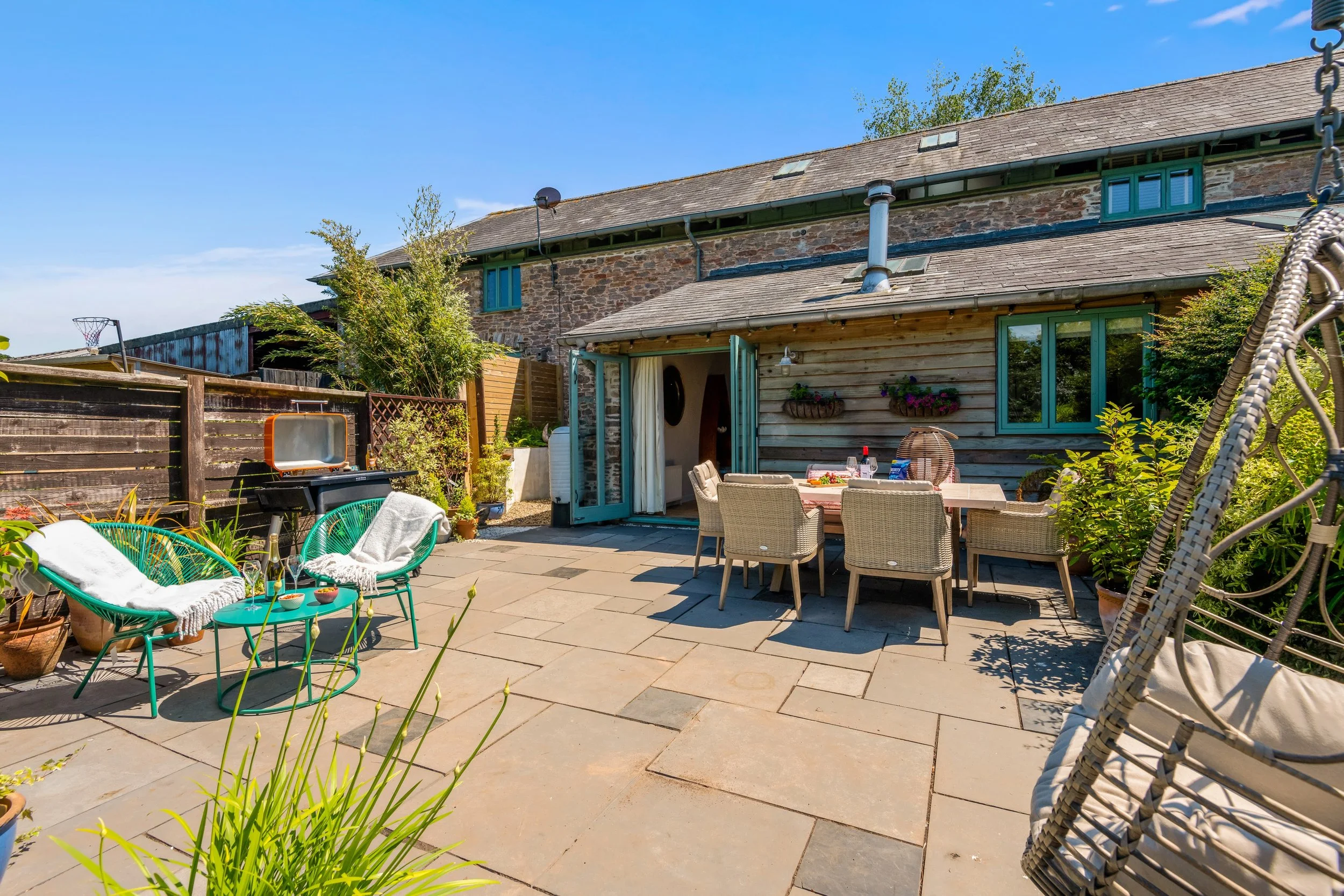 Sunny backyard patio with outdoor furniture, plants, and a brick and wood house exterior.