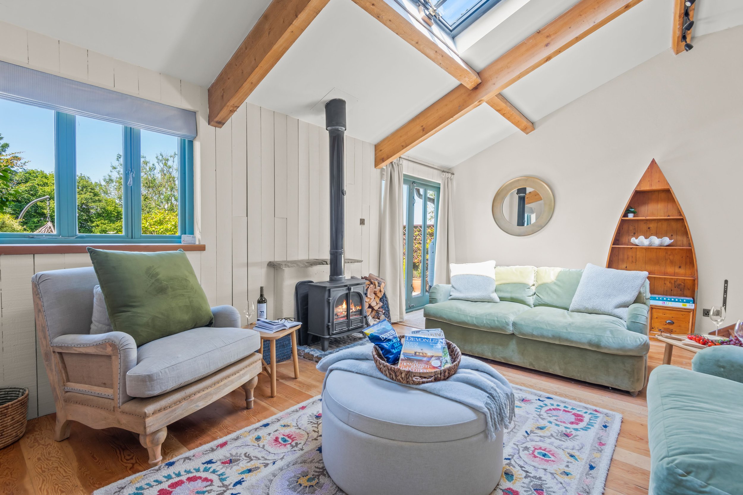 Living room with a wood stove, large windows, and light-colored furniture, including a green sofa and a white armchair, with a sliding glass door leading outside.