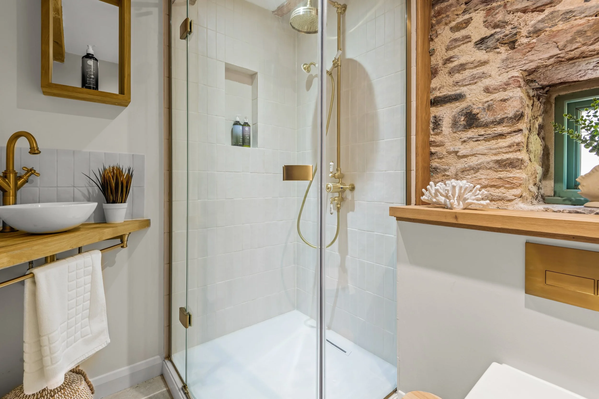 A bathroom with a glass shower enclosure, a wooden countertop with a sink, and decorative items including a plant and a shell on the window ledge.