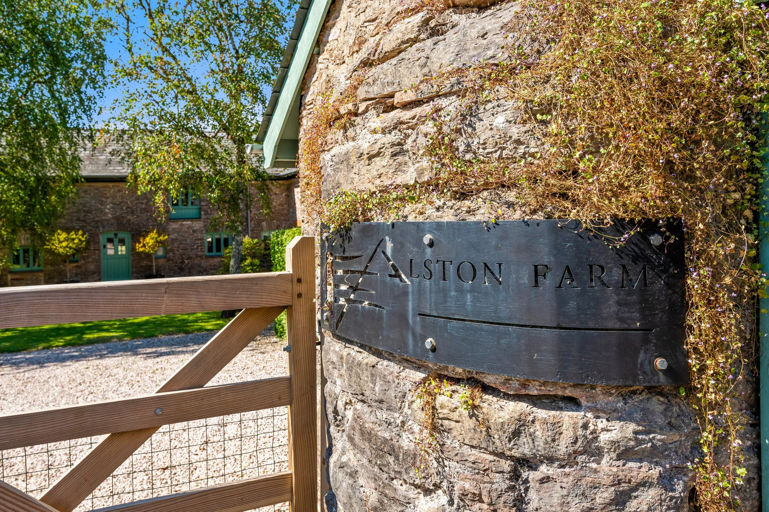 A sign reading 'Aston Farm' attached to a stone wall, with greenery and trees in the background.