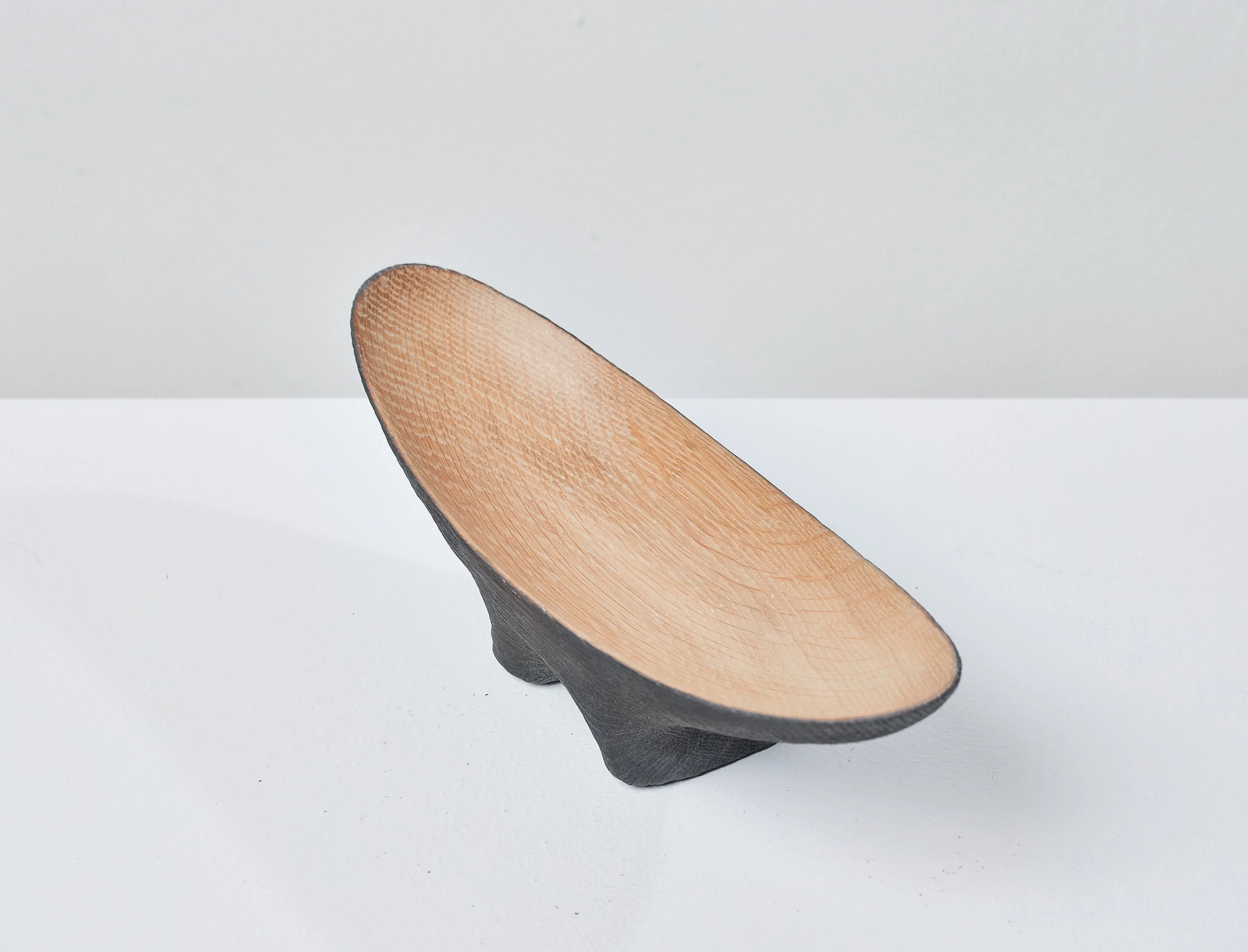 A wooden bowl made from a salvaged oak beam, with a black exterior and a natural wood interior, placed on a white surface against a plain gray background.