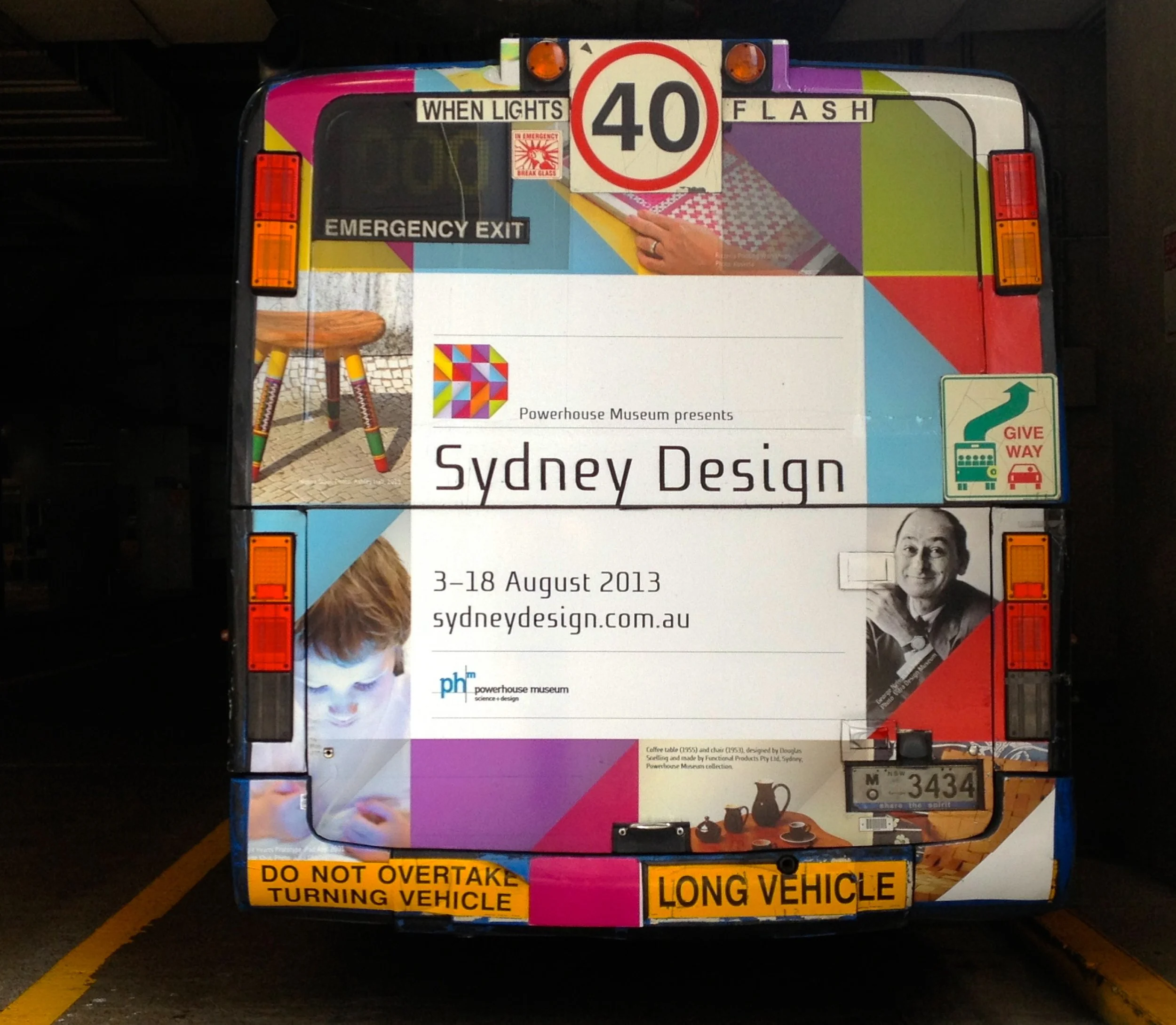 The back of a colorful bus with advertisements for Sydney Design, an exhibition at Powerhouse Museum featuring a picture of the Nironi stool by Matt Kavanagh