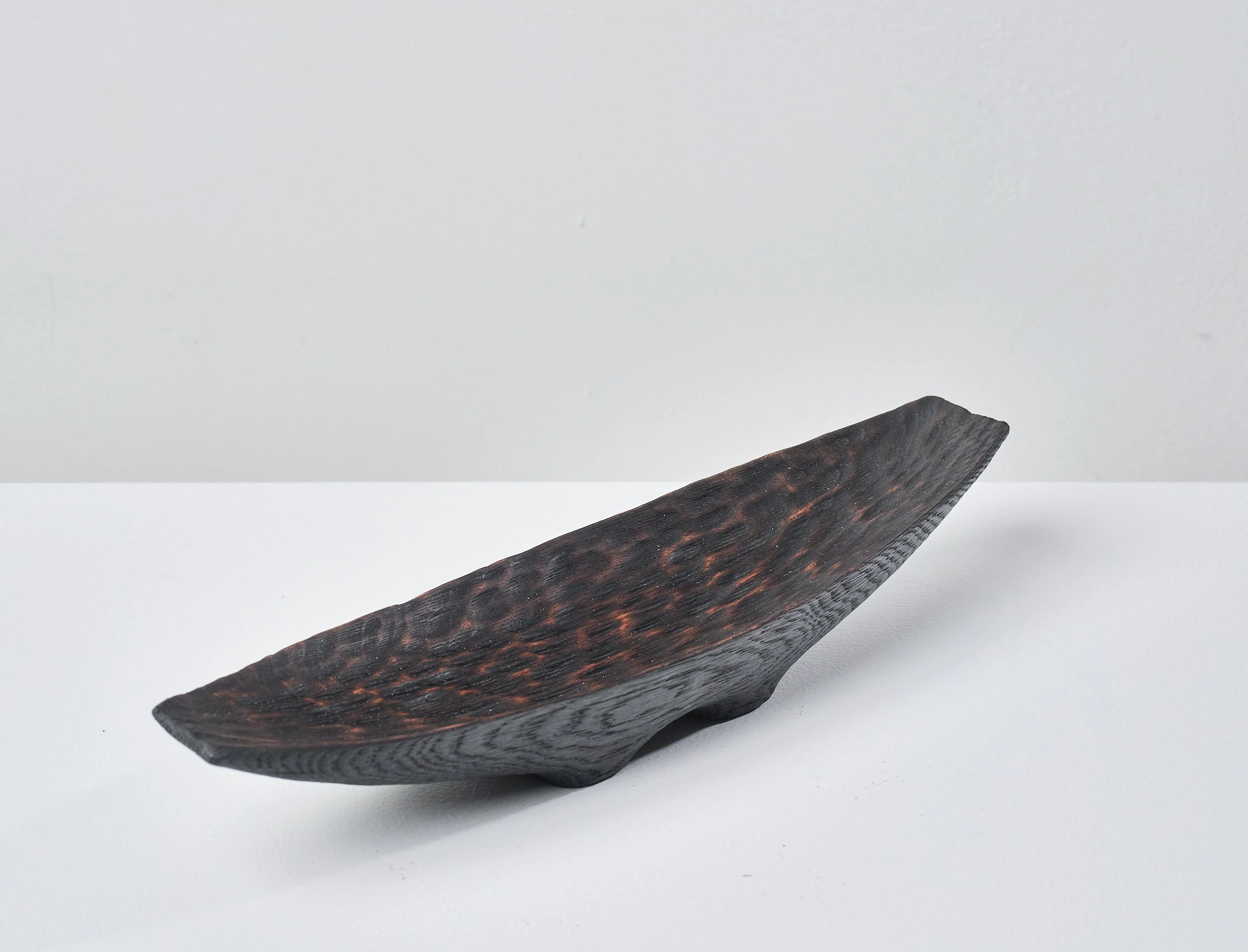 Wooden trough made from an ancient oak beam. The textured surface is charred, waxed and polished. It sits on a white surface against a light grey background.