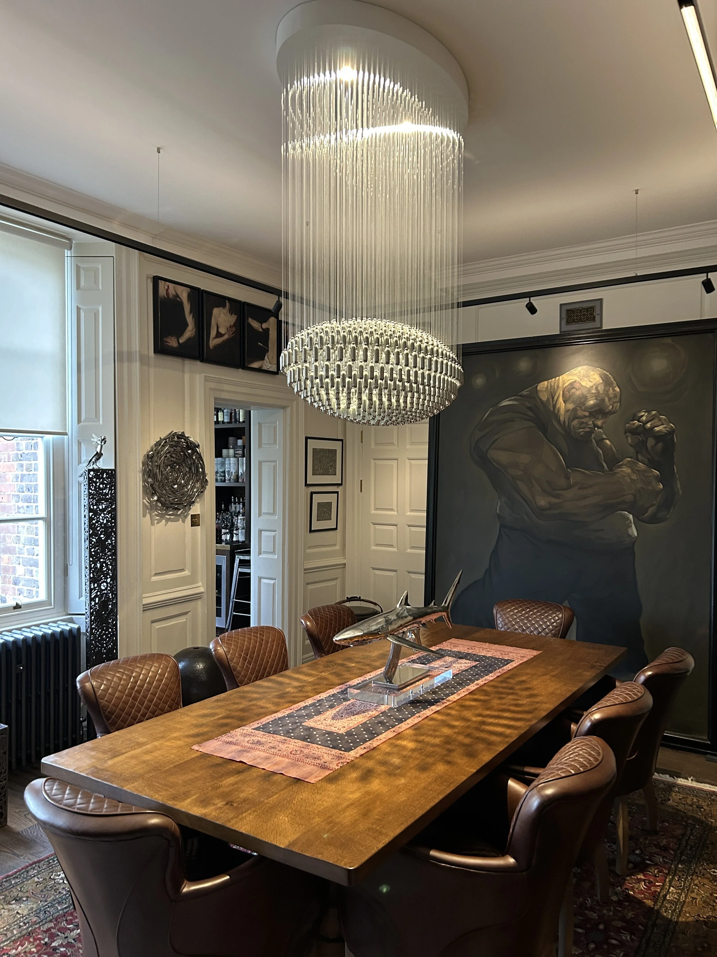 Elegant dining room  in a luxury interior with a specially commissioned, large bespoke oval NOS Sphere chandelier hanging from ceiling, wooden dining table with framed artwork on the walls.