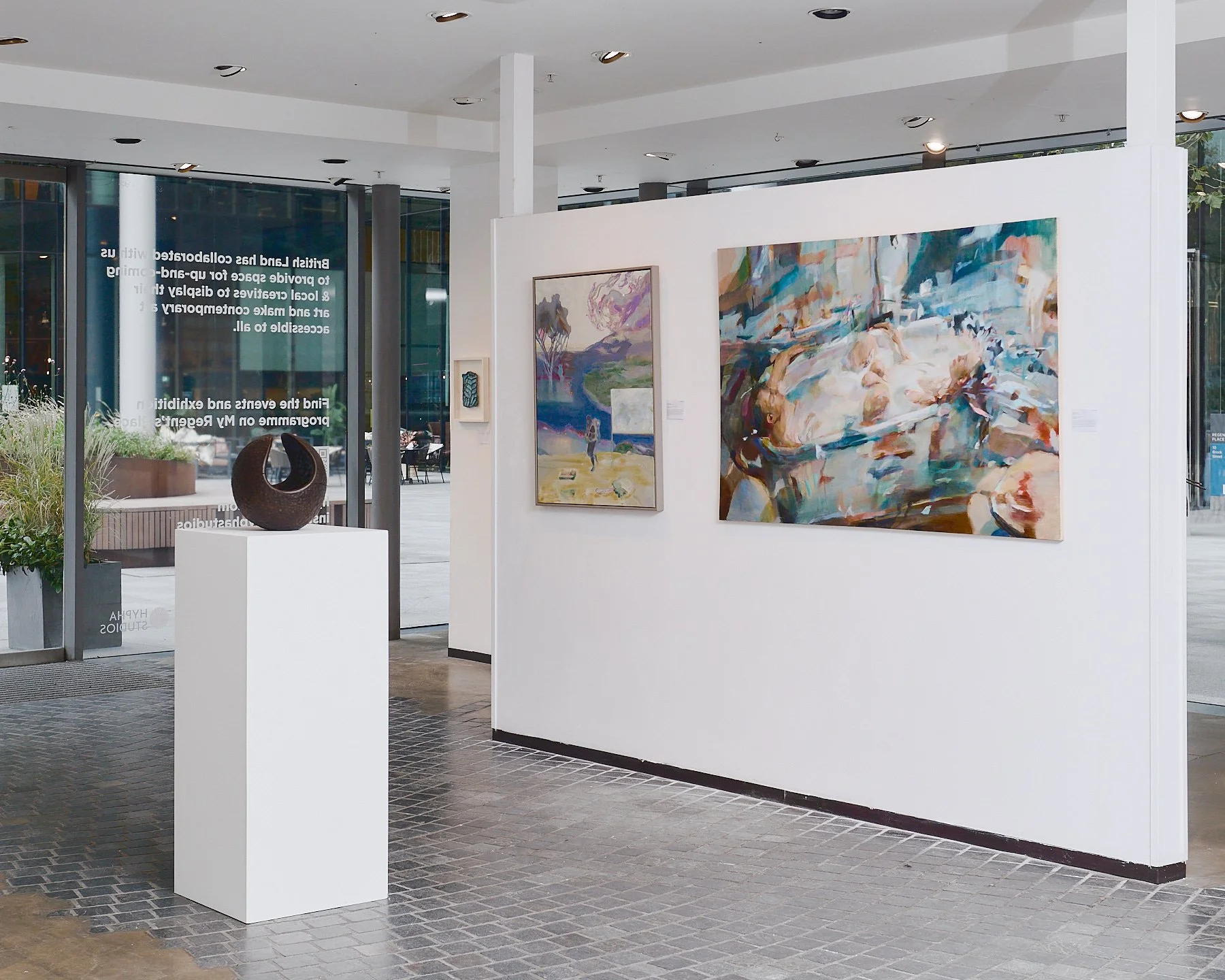Interior of the Hypha Curates art gallery featuring London Plane Sphere by Matt Kavanagh, part of the Coordinates collection of craft made unique functional sculpture, carved from urban fallen trees. Paintings are on the wall behind.