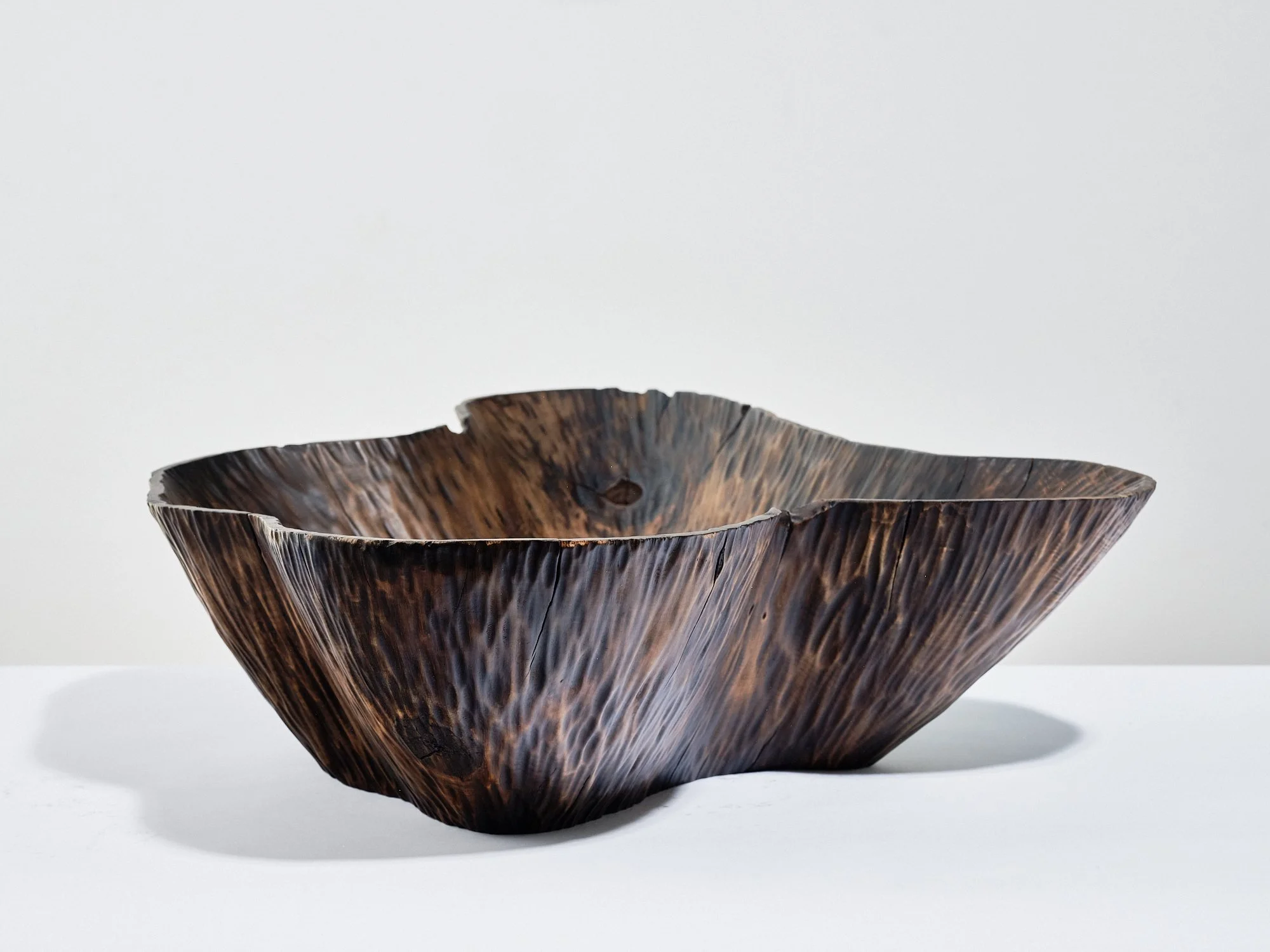 A dark conker brown, textured, organic-shaped wooden bowl made from horse chestnut, on a white surface against a plain white background.