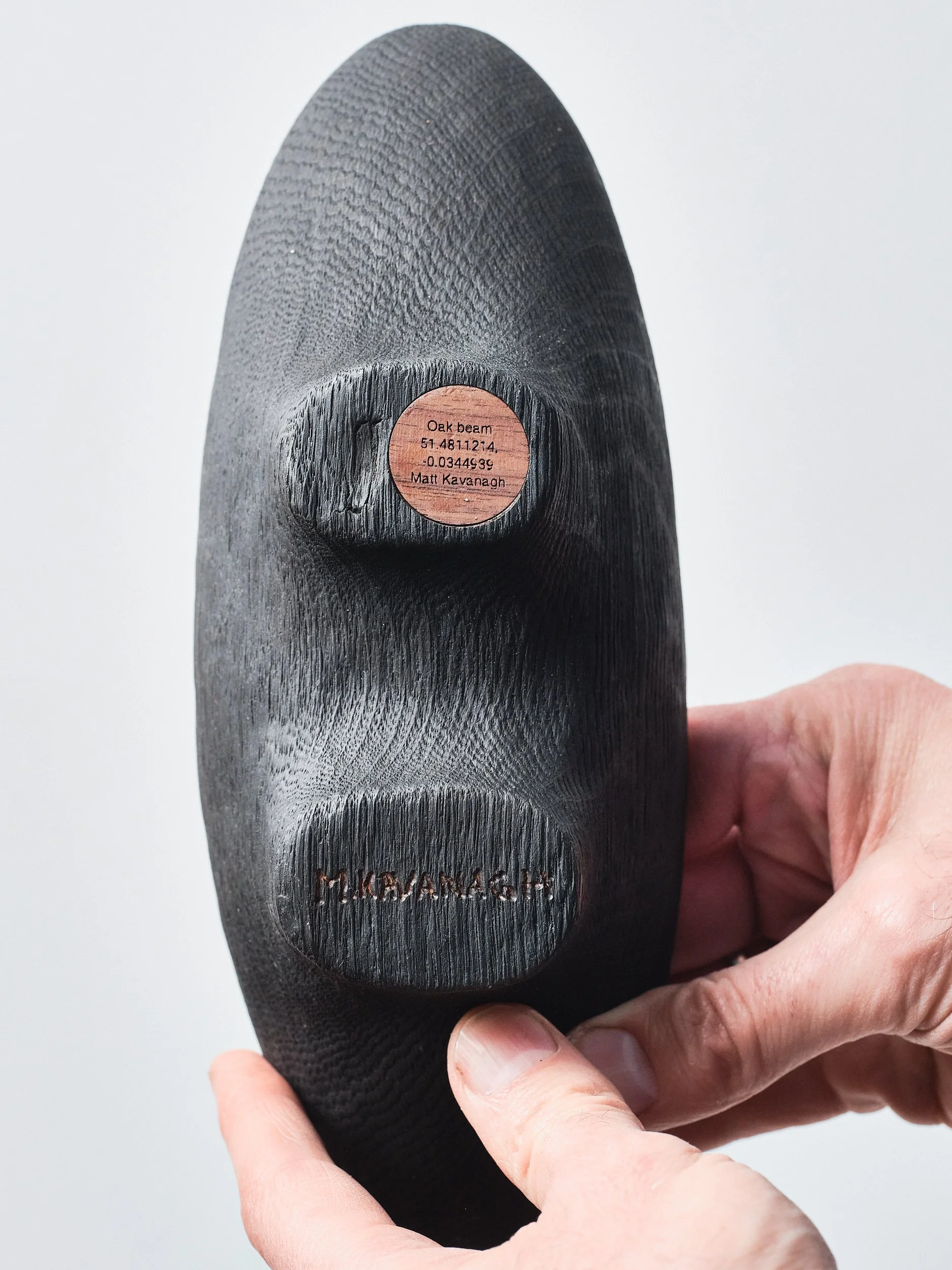 Close up of the underside of the Oak Beam dish showing the brushed black base with visible grain and a badge with timber species, coordinates of where the beam was sourced and the artists signature
