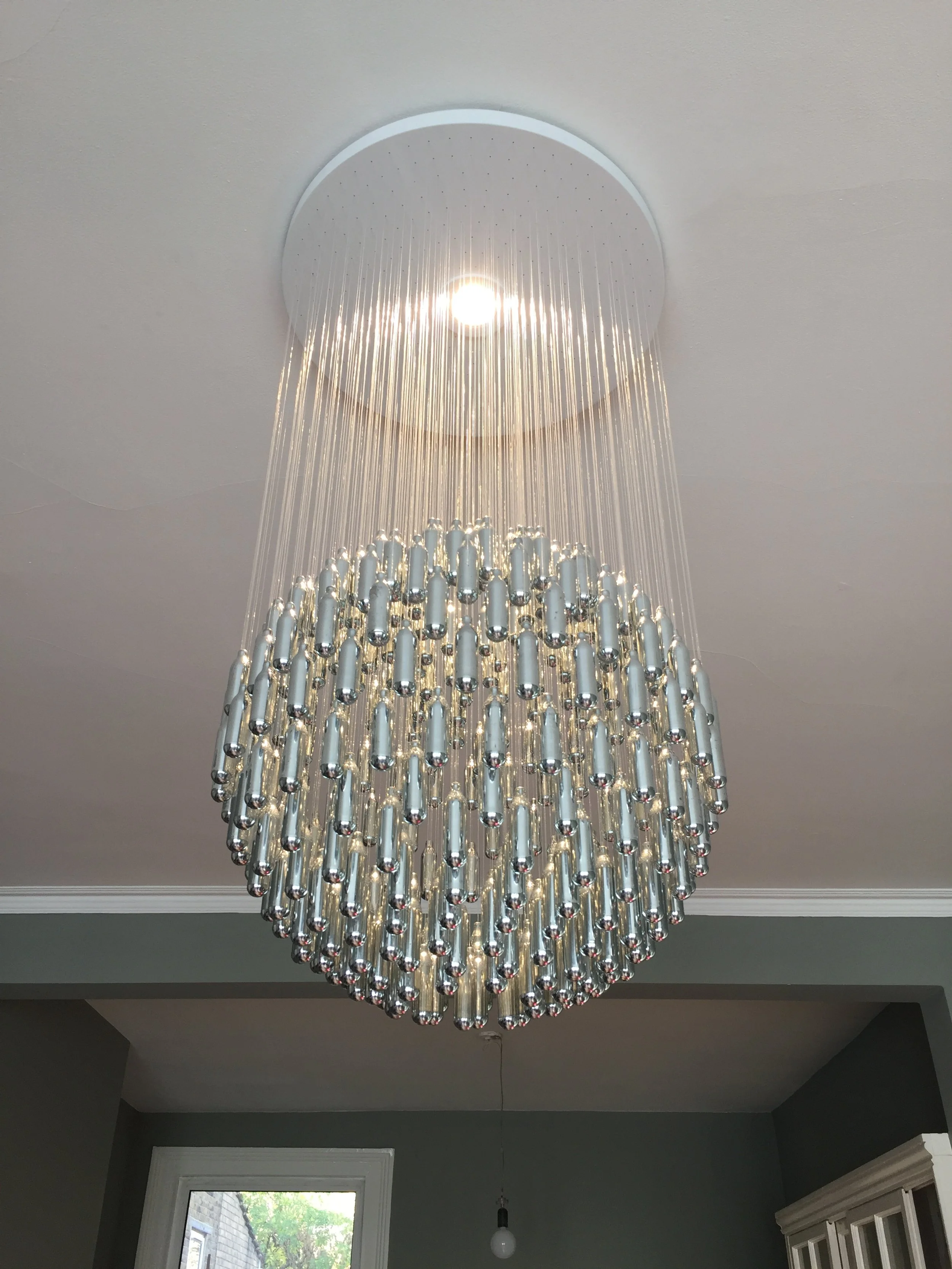 A large, elegant, NOS Sphere 348 chandelier made from discarded nitrous oxide canisters gathered in South London and repurposed, machined and polished to create a cloud of reflections in a domestic living room