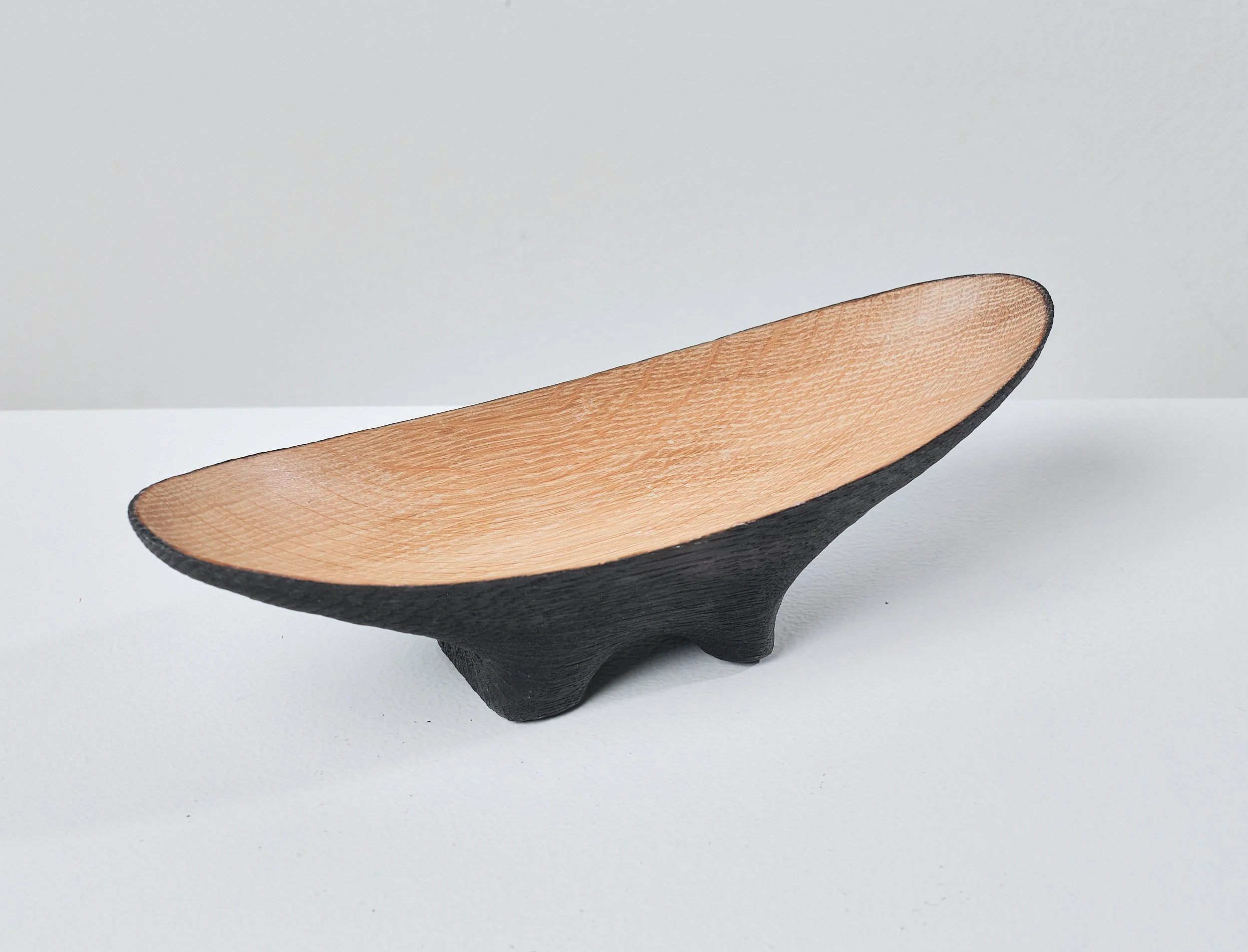A wooden bowl made from a salvaged oak beam, with a black exterior and a natural wood interior, placed on a white surface against a plain gray background.