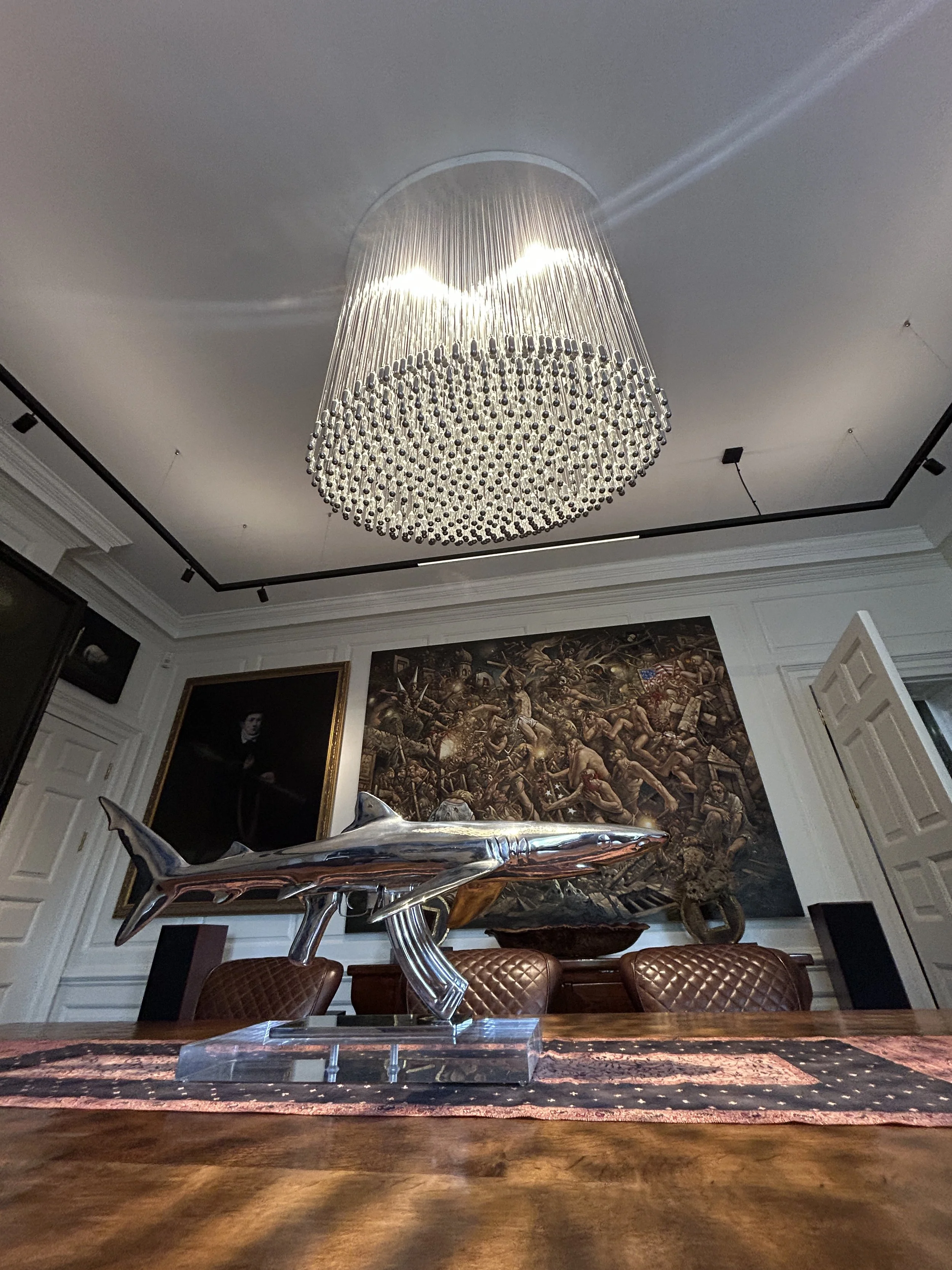 Elegant dining room  in a luxury interior with a specially commissioned, large bespoke oval NOS Sphere chandelier hanging from ceiling, wooden dining table with framed artwork on the walls.