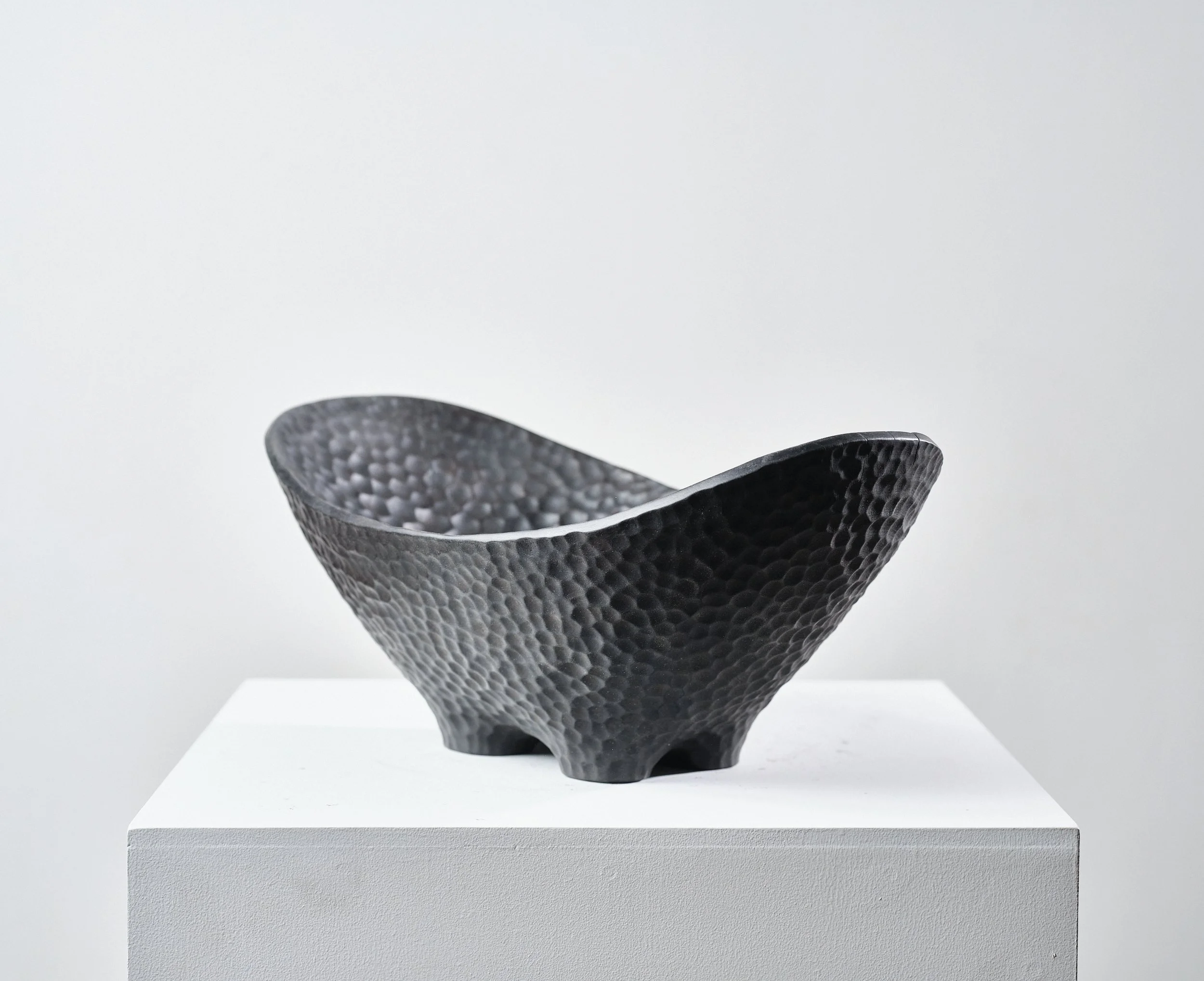 Black textured long bowl made from London Plane timber, on white pedestal in a gallery setting