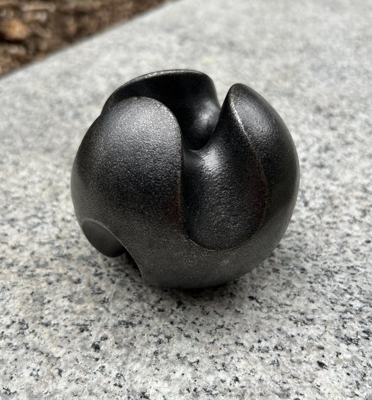 Close-up of Roller Ball, a blackened sand-cast iron candle holder, placed on a grey concrete surface.