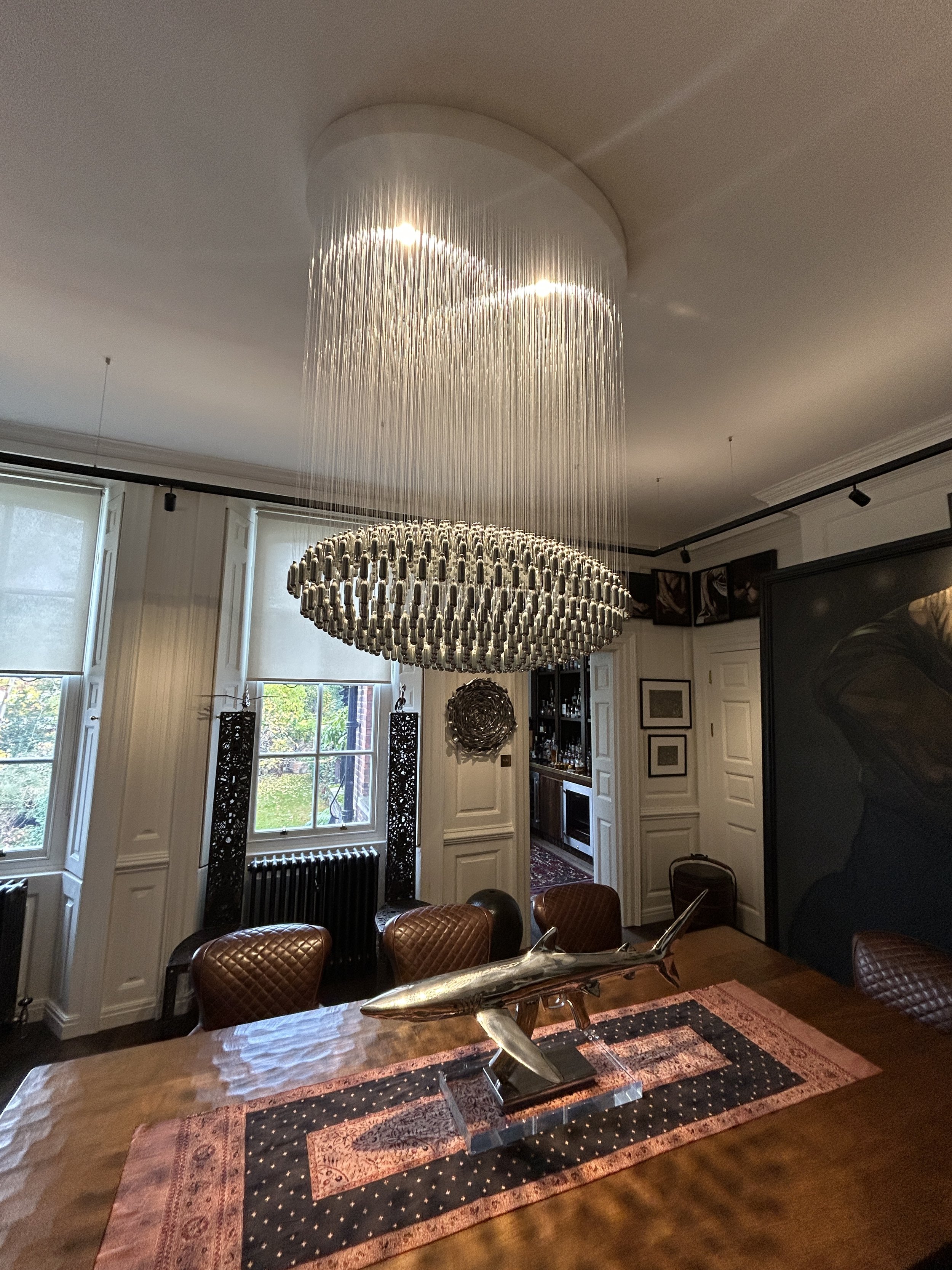 Elegant dining room  in a luxury interior with a specially commissioned, large bespoke oval NOS Sphere chandelier hanging from ceiling, wooden dining table with framed artwork on the walls.