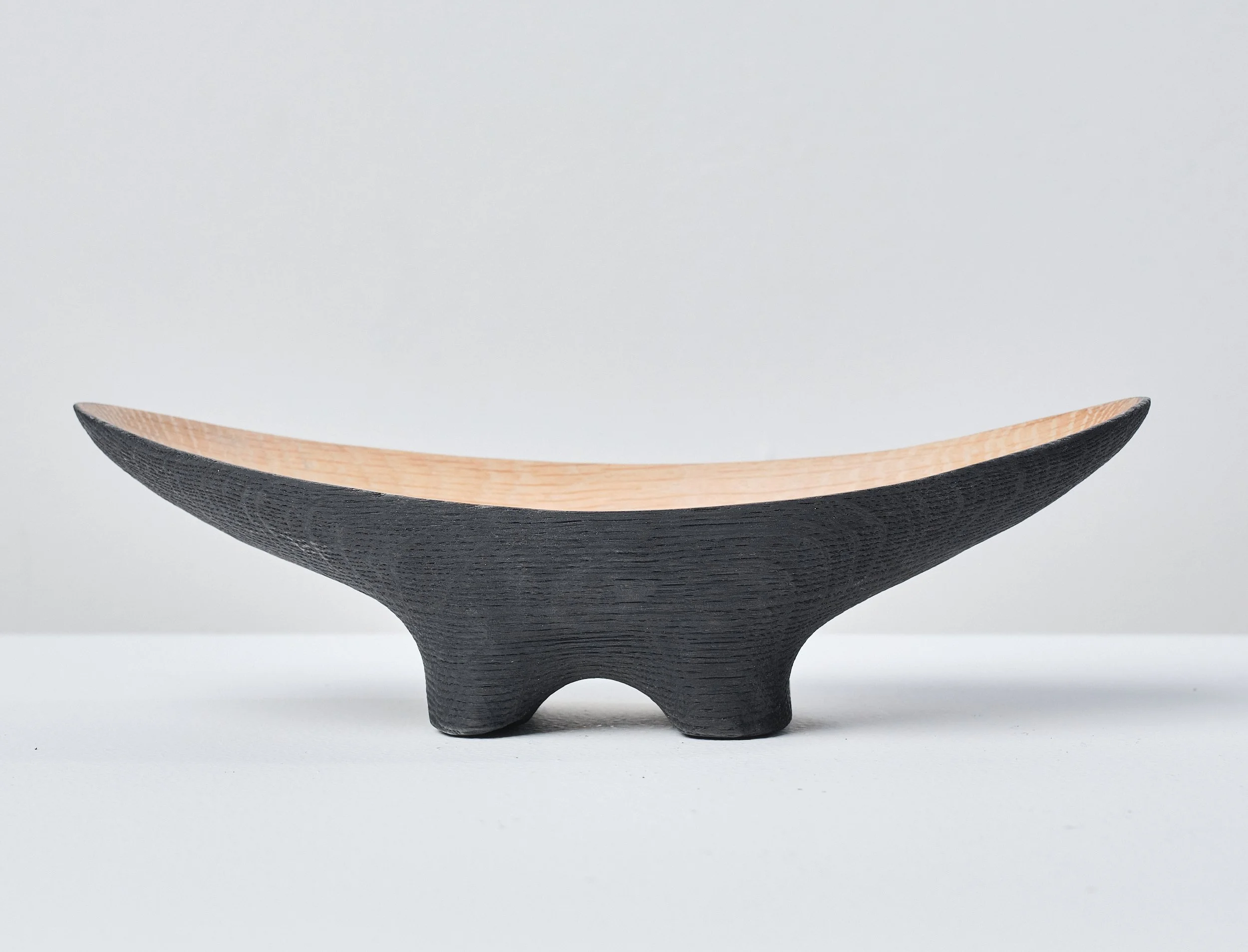 A wooden bowl made from a salvaged oak beam, with a black exterior and a natural wood interior, placed on a white surface against a plain gray background.