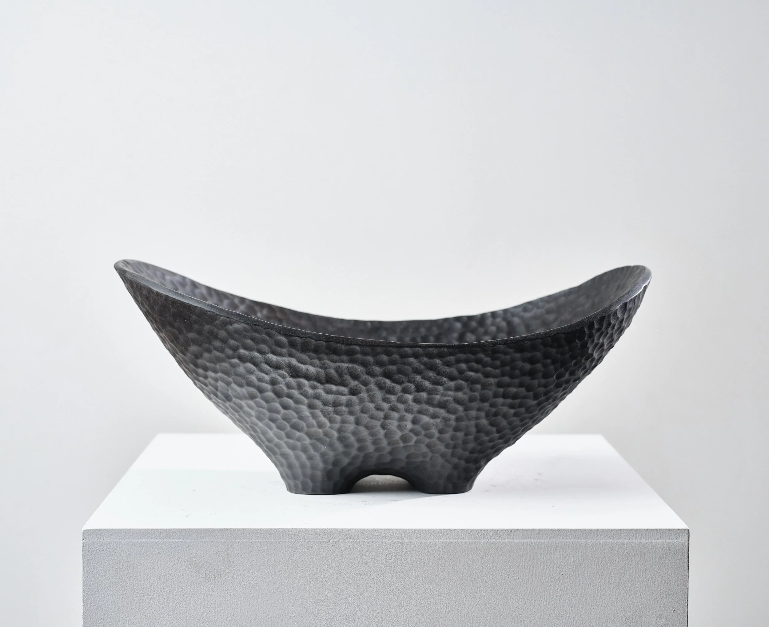 Black textured long bowl made from London Plane timber, on white pedestal in a gallery setting