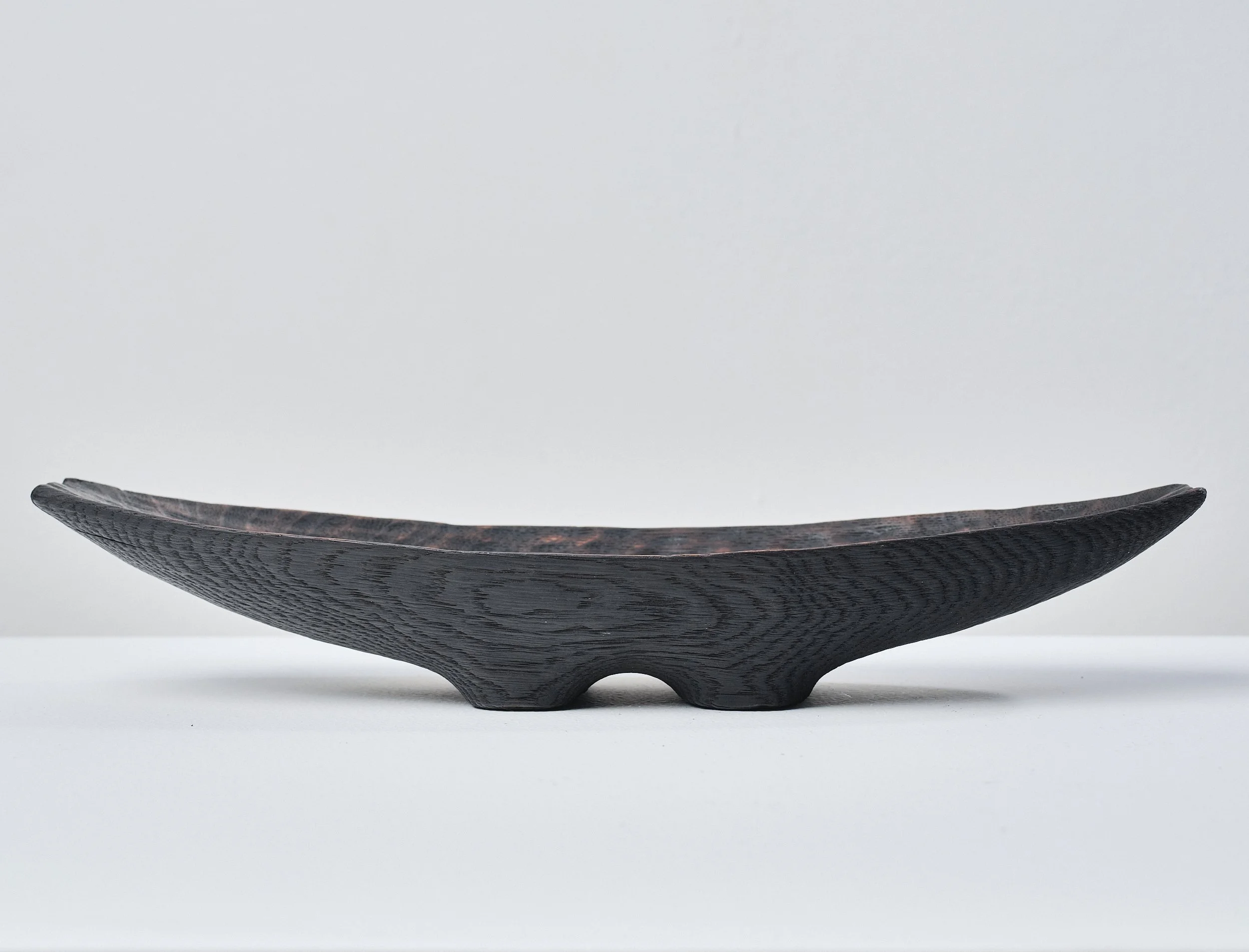 Side view of a wooden trough made from an ancient oak beam. The textured surface is charred, waxed and polished. It sits on a white surface against a light grey background.