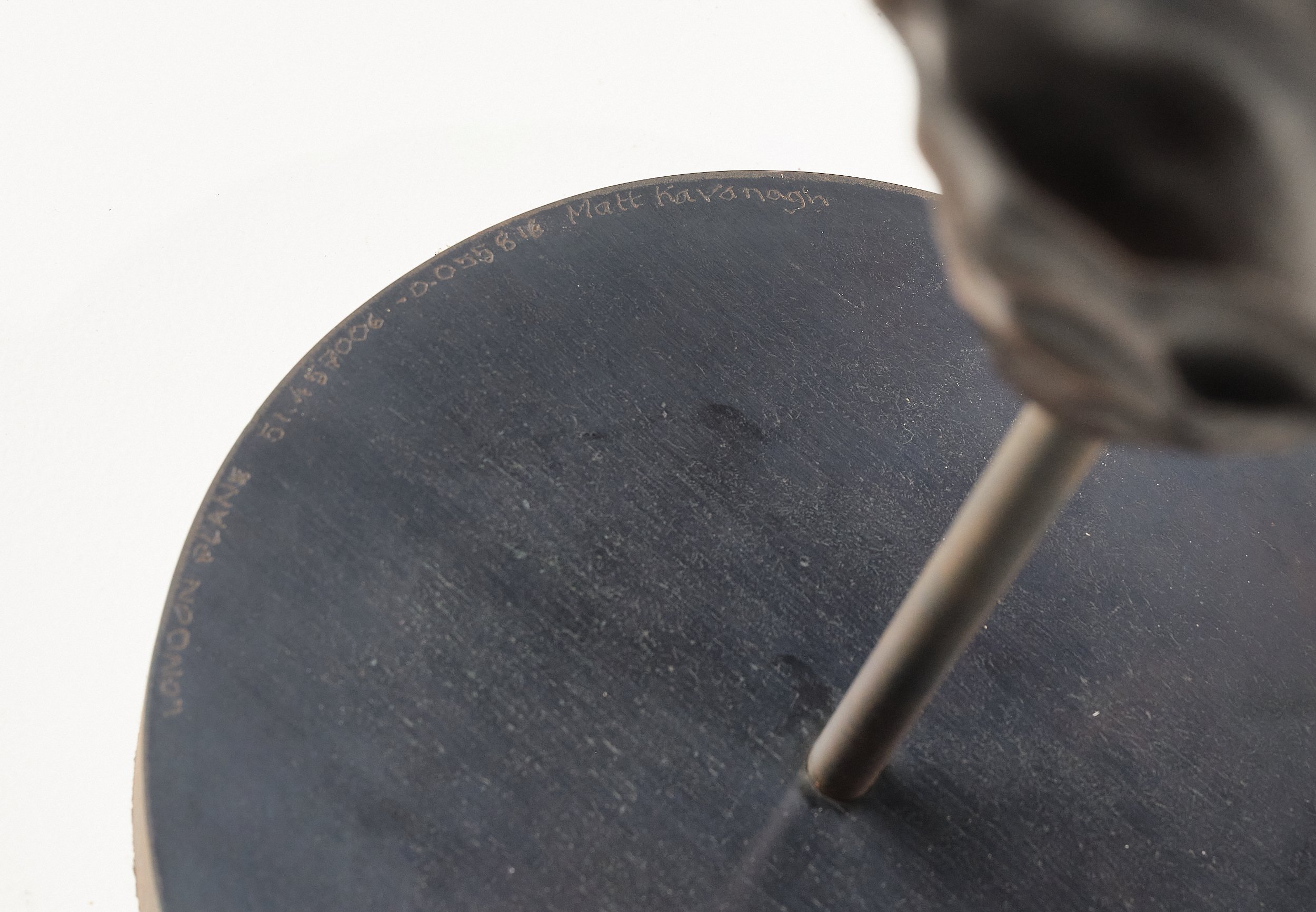 Close-up detail of a black disc base to a sculpture engraved with the artist's signature and coordinates of the location of the London Plane tree that the sculpture was carved from.
