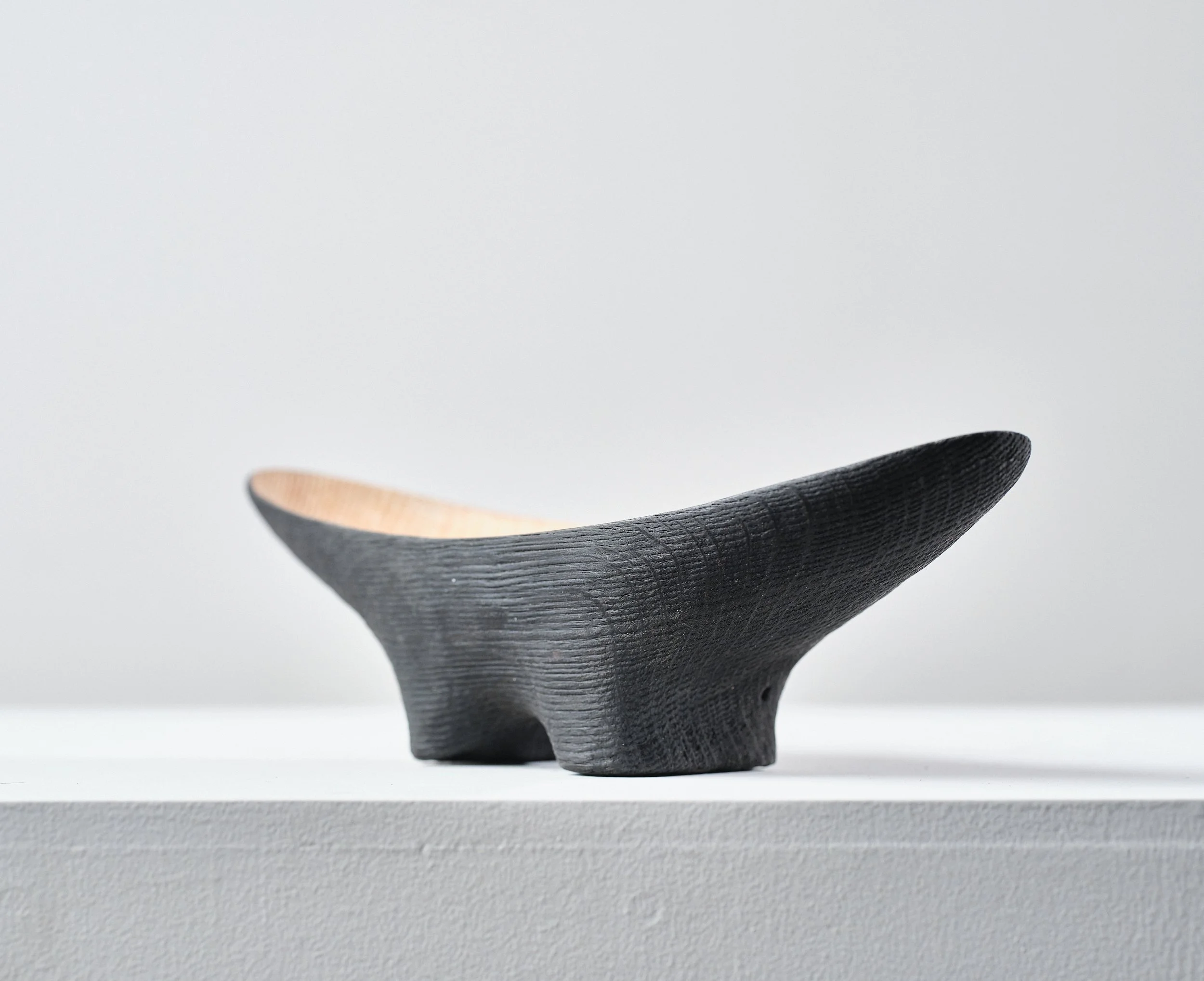 Black burned and wire brushed oak dish with natural wood interior, has a smooth, curved shape and two legs, placed on a white surface against a plain white background.