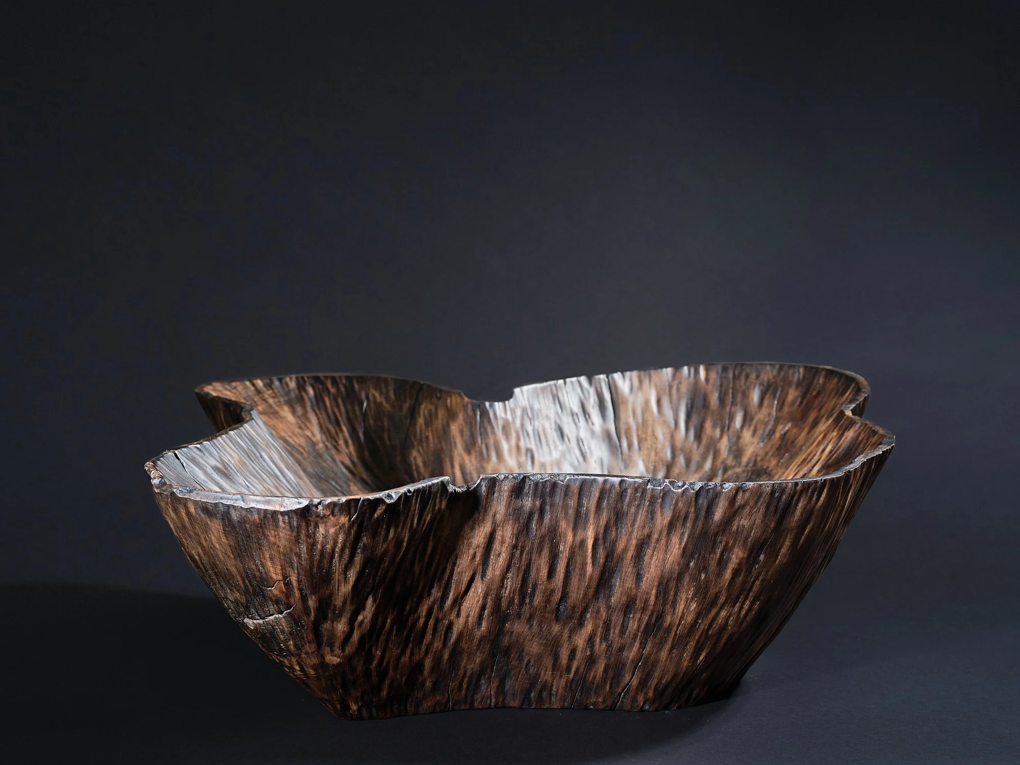 A dark conker brown, textured, organic-shaped wooden bowl made from horse chestnut against a plain black background.