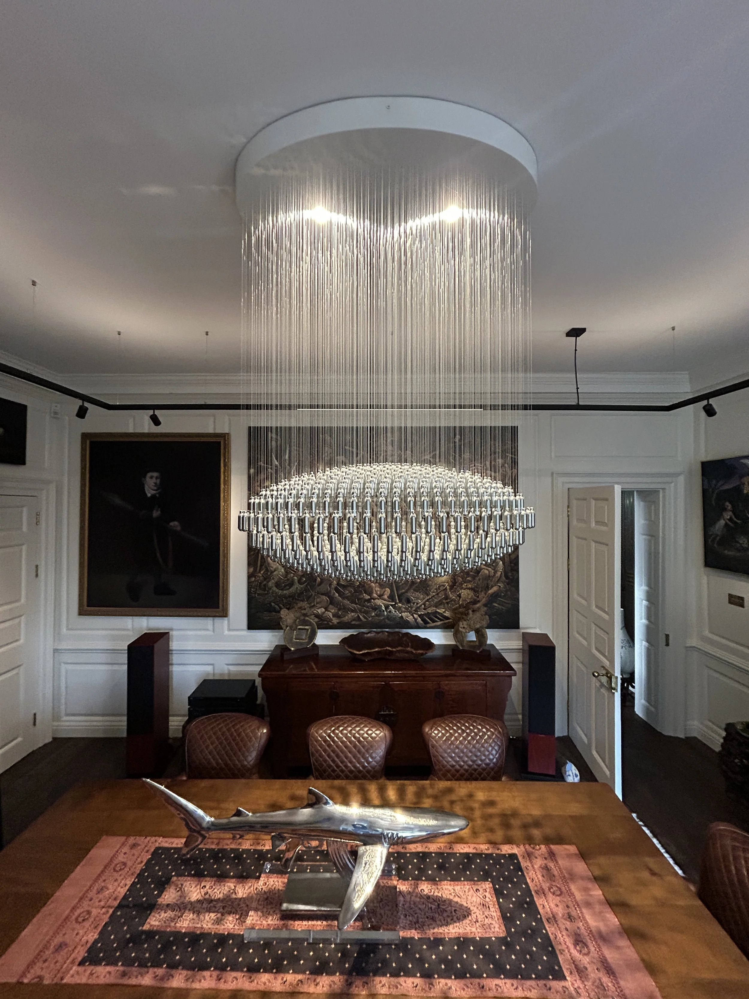 Elegant dining room  in a luxury interior with a specially commissioned, large bespoke oval NOS Sphere chandelier hanging from ceiling, wooden dining table with framed artwork on the walls.