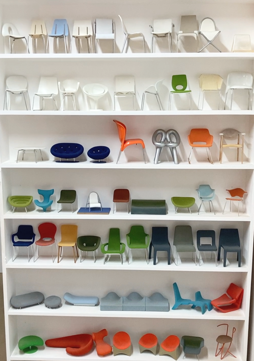 Display wall with white shelves of 1:5 scale models of contemporary chair designs