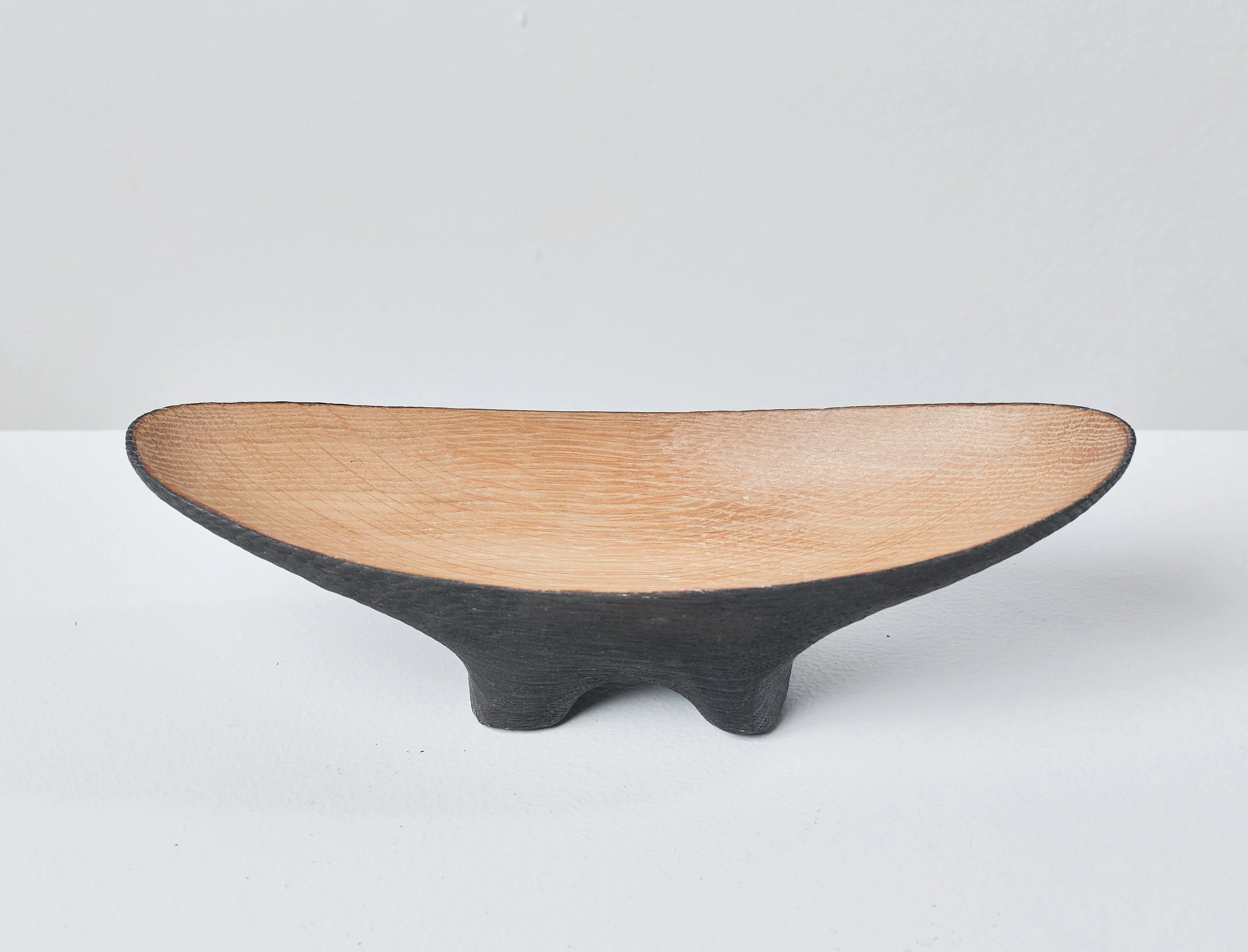 A decorative wooden dish with a dark exterior and a natural oak interior, resting on a white surface against a plain background.