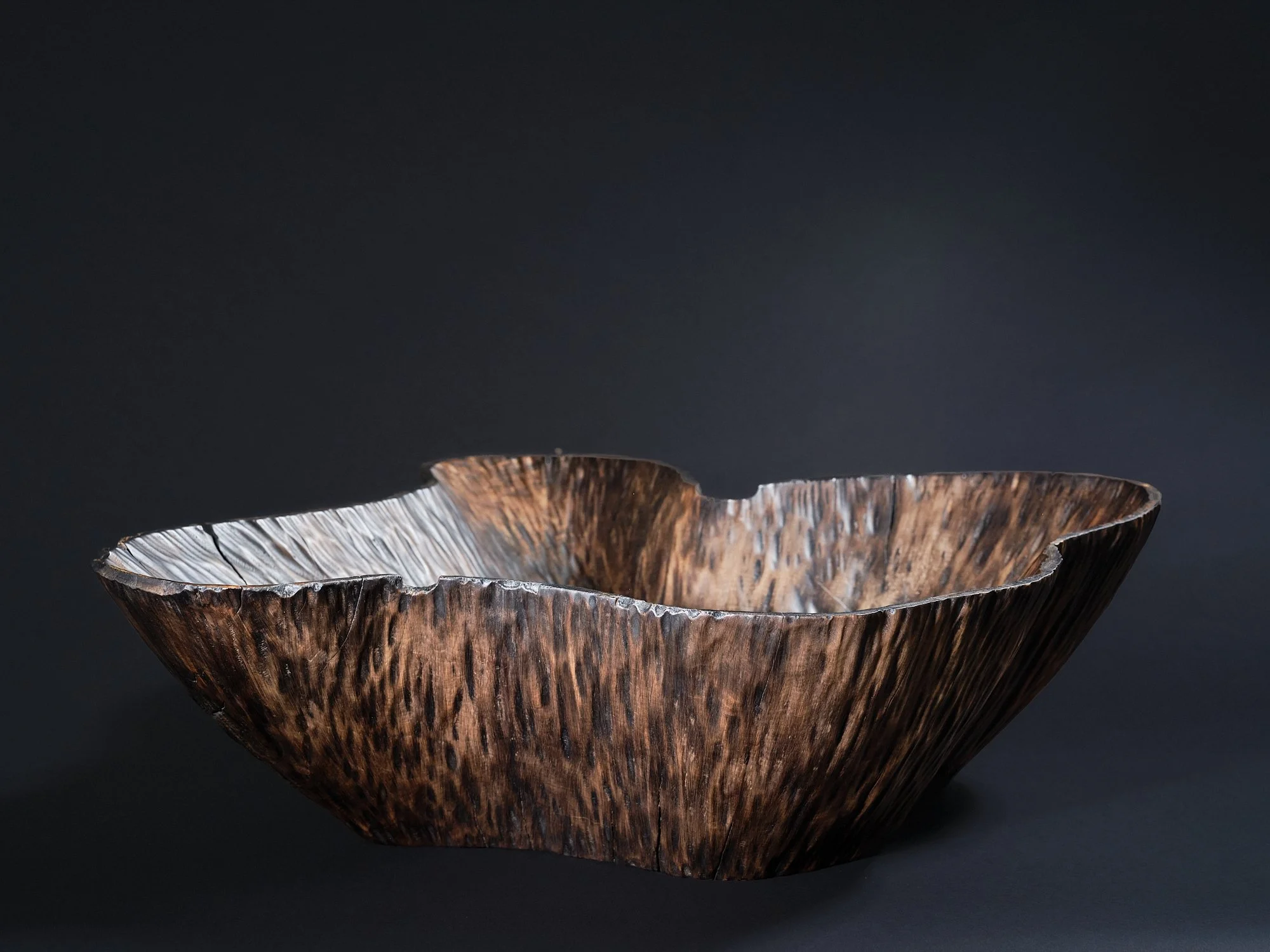 A dark conker-brown, rib-textured, organic-shaped wooden bowl made from horse chestnut, on a black background.