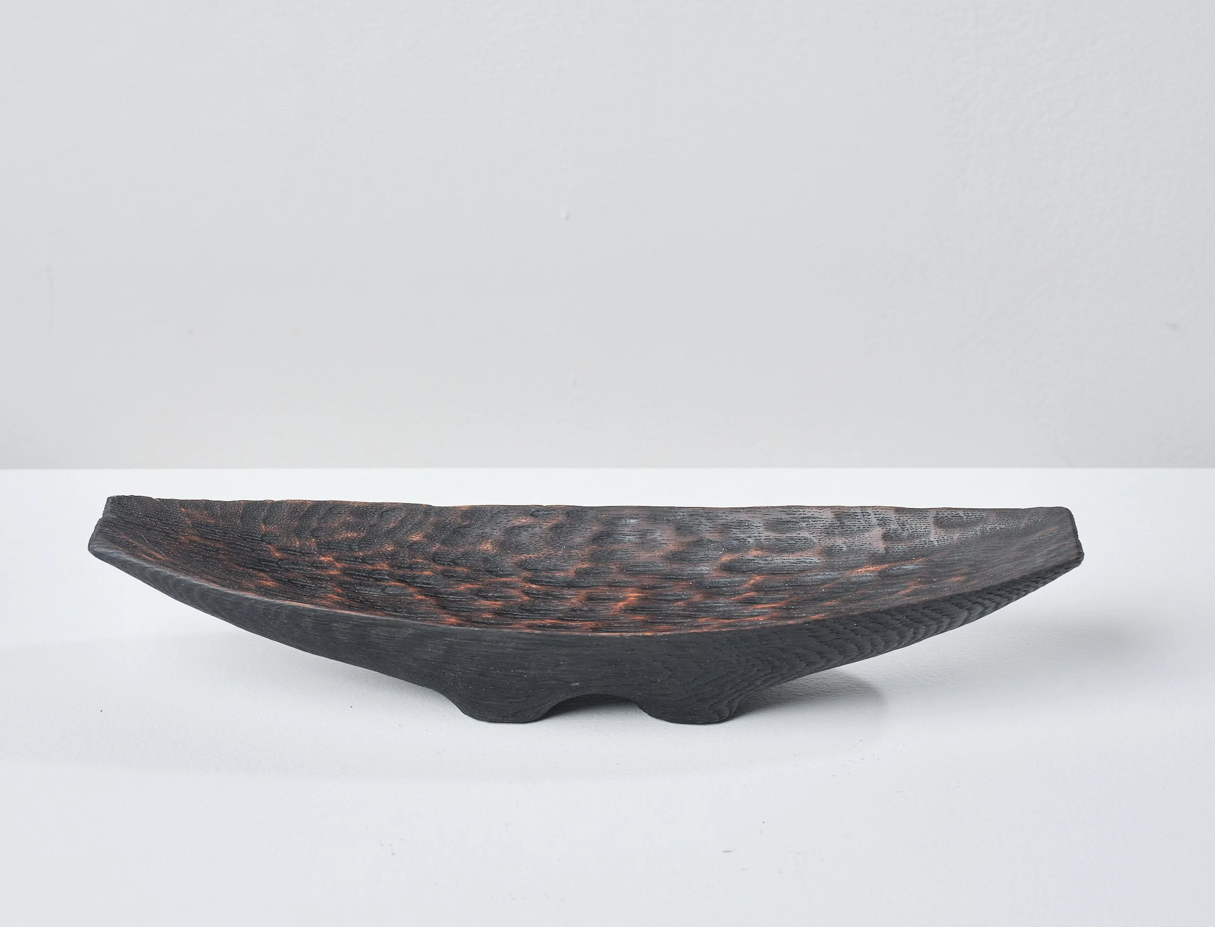 Wooden trough made from an ancient oak beam. The textured surface is charred, waxed and polished. It sits on a white surface against a light grey background.