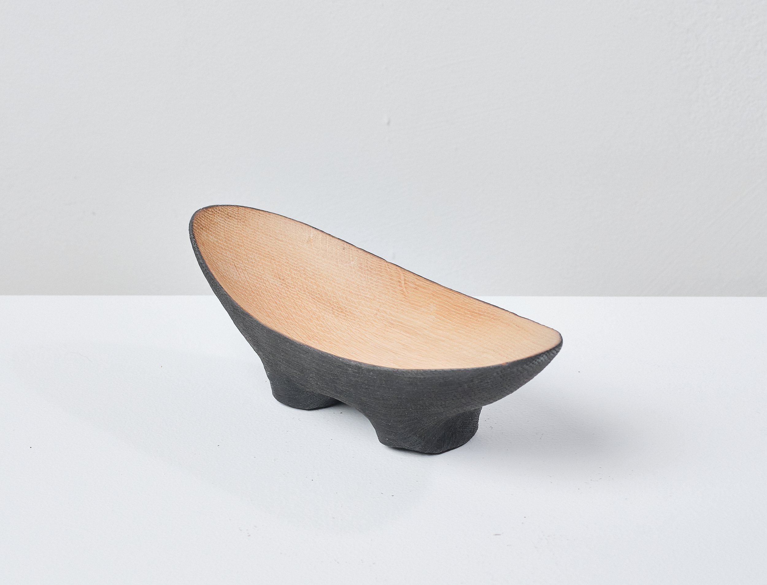 A wooden bowl made from a salvaged oak beam, with a black exterior and a natural wood interior, placed on a white surface against a plain grey background.