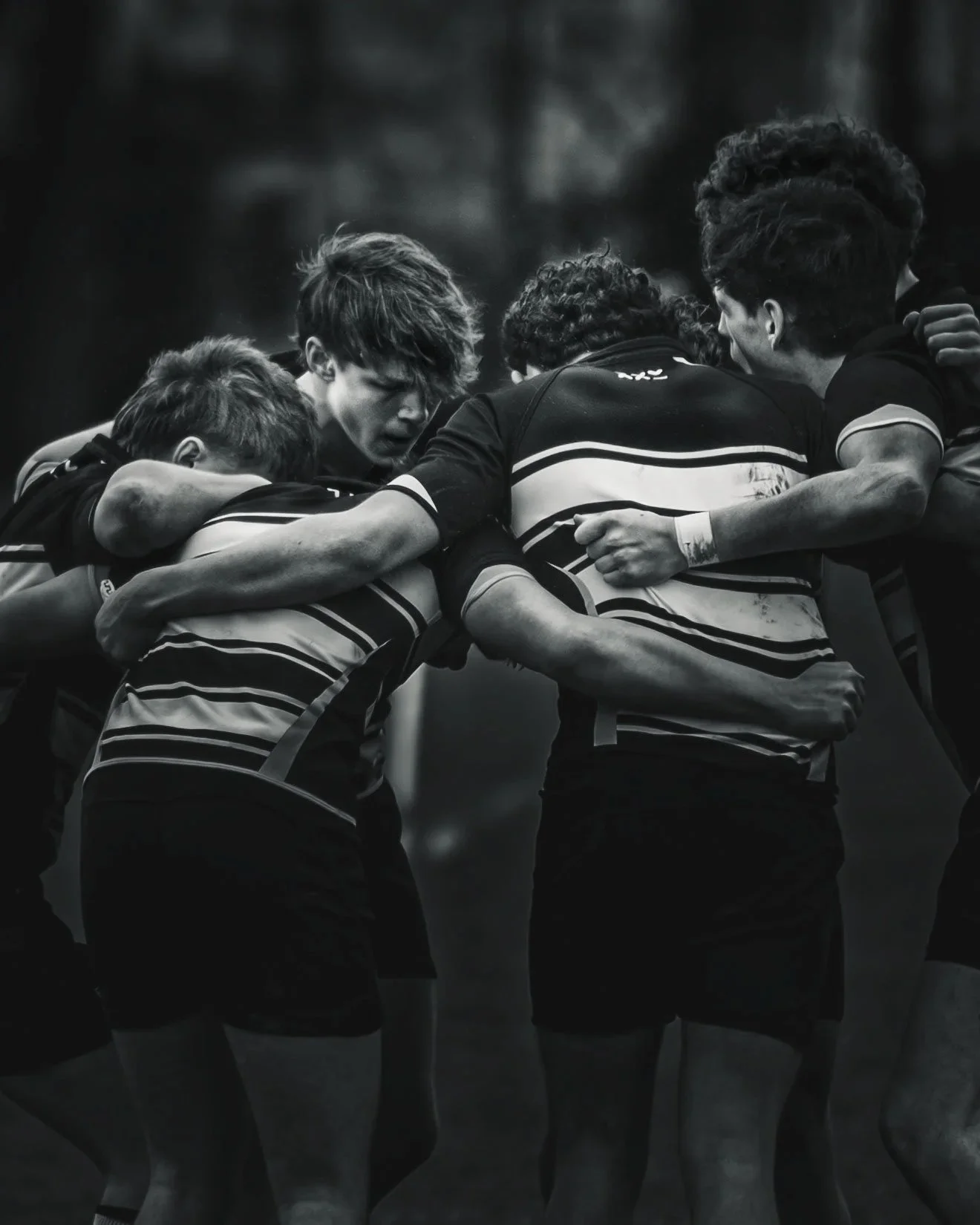 A group of rugby players in a huddle on the field, shows teamwork and focus.