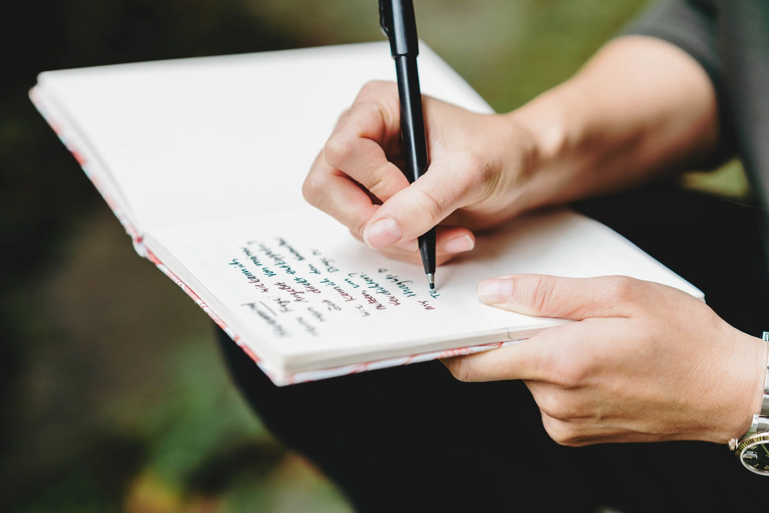 Lea Im Obersteg writing in a notebook with a black pen, with handwritten notes visible on the pages. This symbolizes her regular work on blog posts about Connections meant to be in life and business via Substack in her blog "Yuanfen - Lea's Stories".
