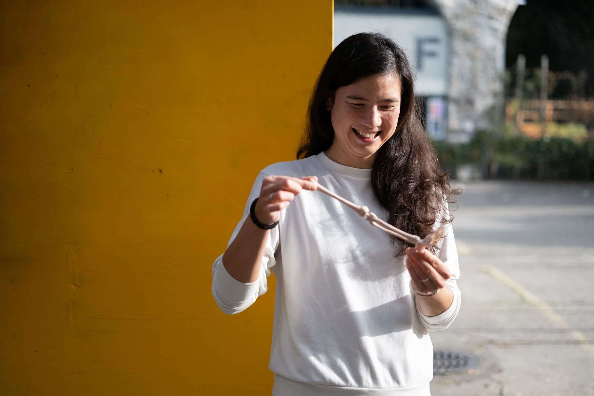 Lea Im Obersteg wearing a white pullover, holding a leg of a plastic skeleton, representing unconventional tools that get applied during her work.