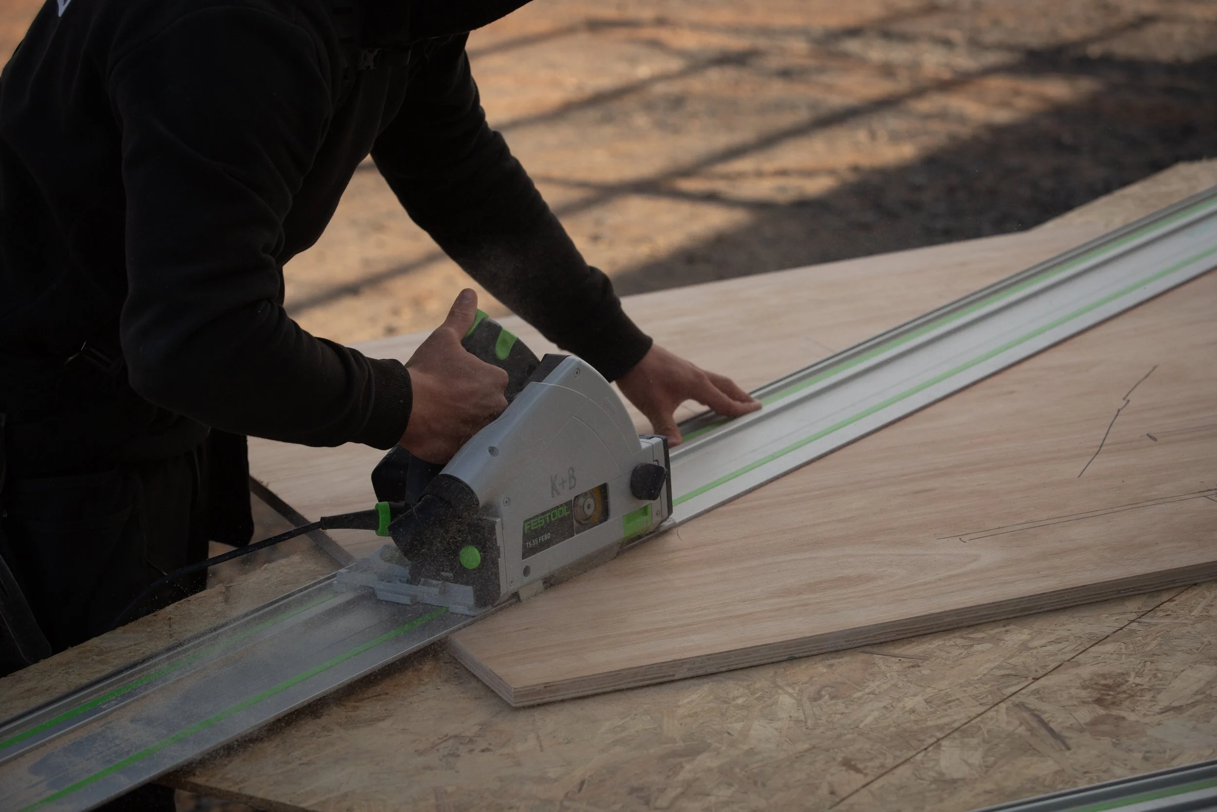 Person using a tool to cut a piece of wood on a workbench outdoors.