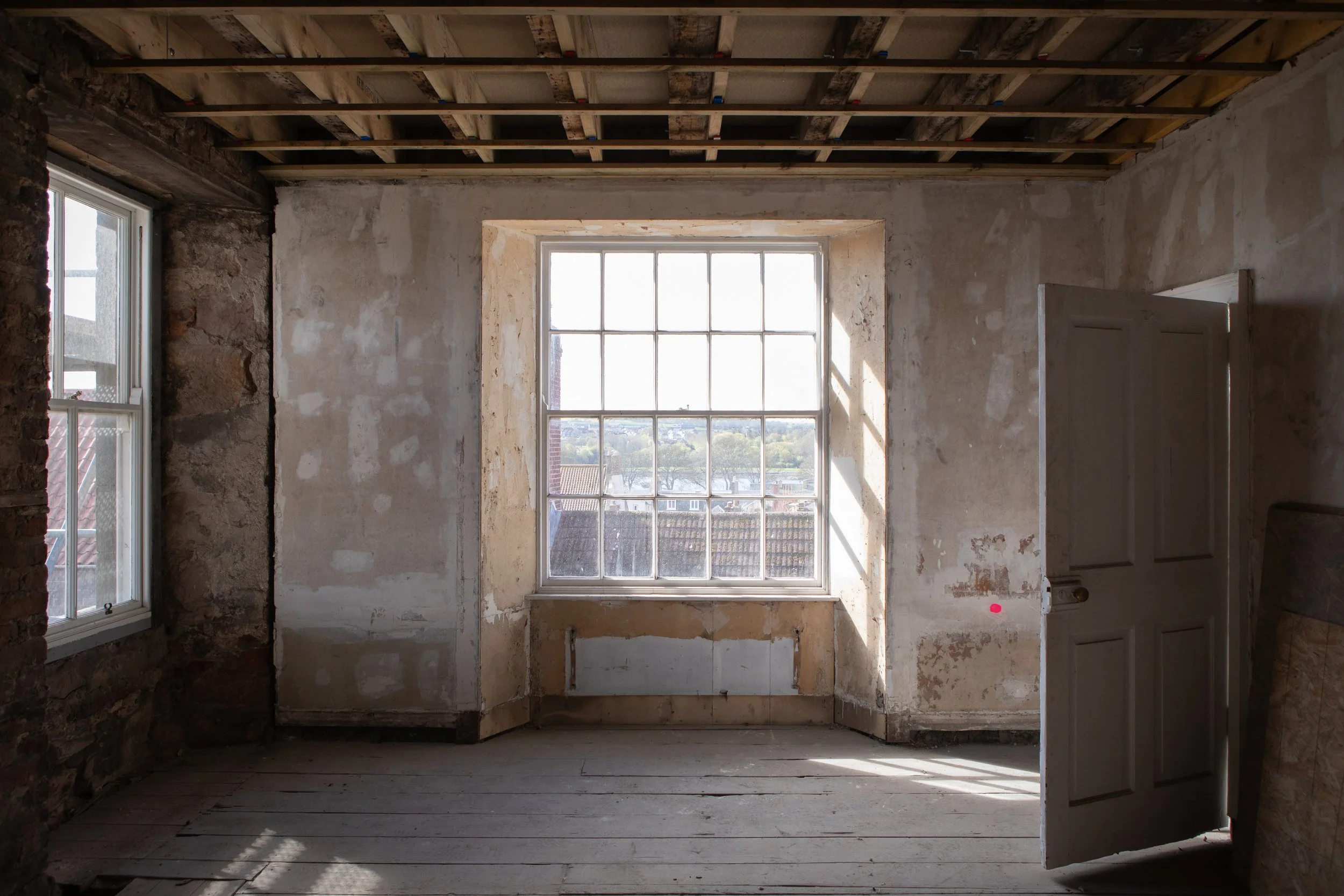 An under-construction room with unfinished walls, a large window, and a wooden floor in progress.