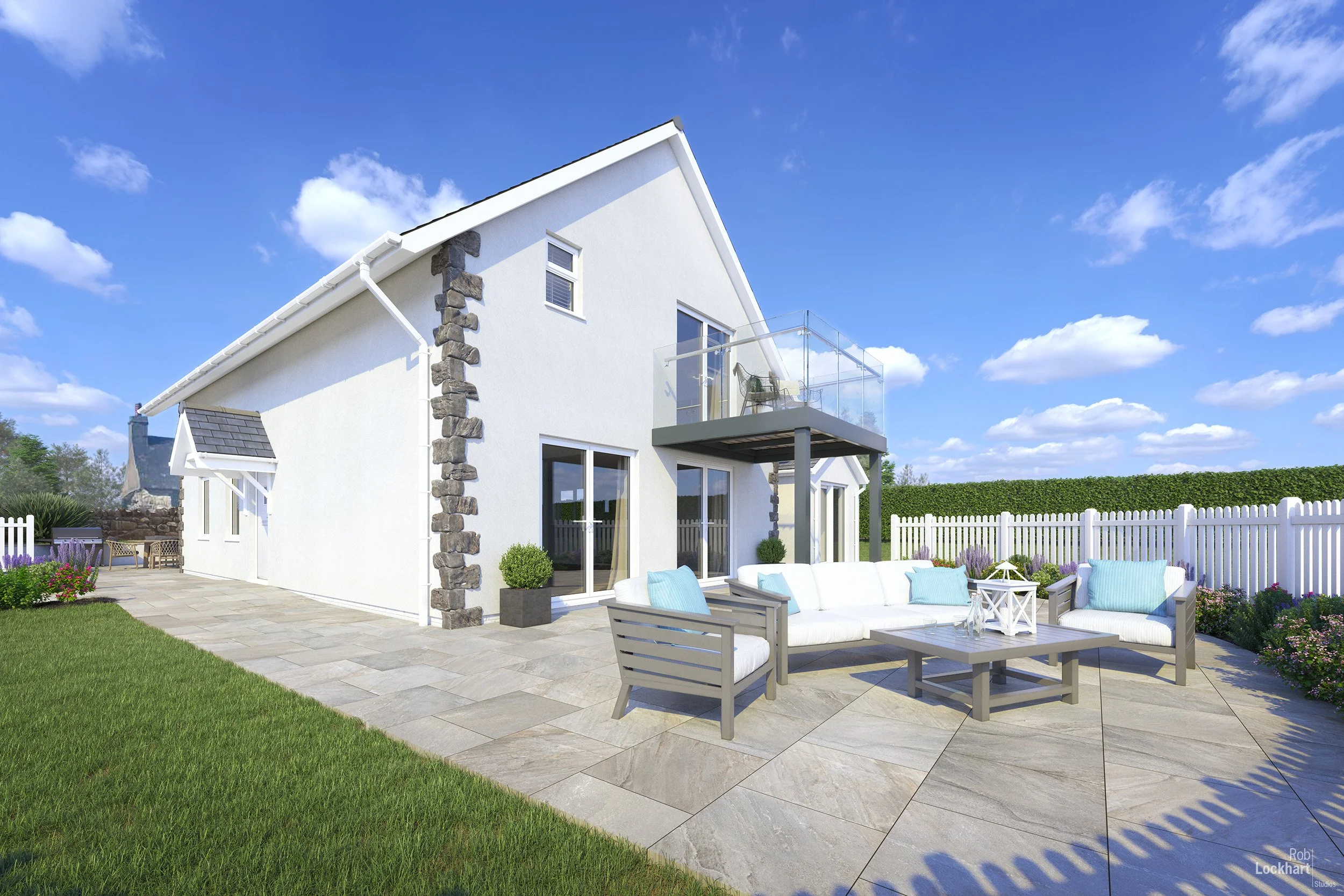 Modern white two-story house with stone accents, glass balcony, and outdoor patio with white seating and blue pillows, surrounded by a green lawn and white picket fence under a blue sky with clouds.